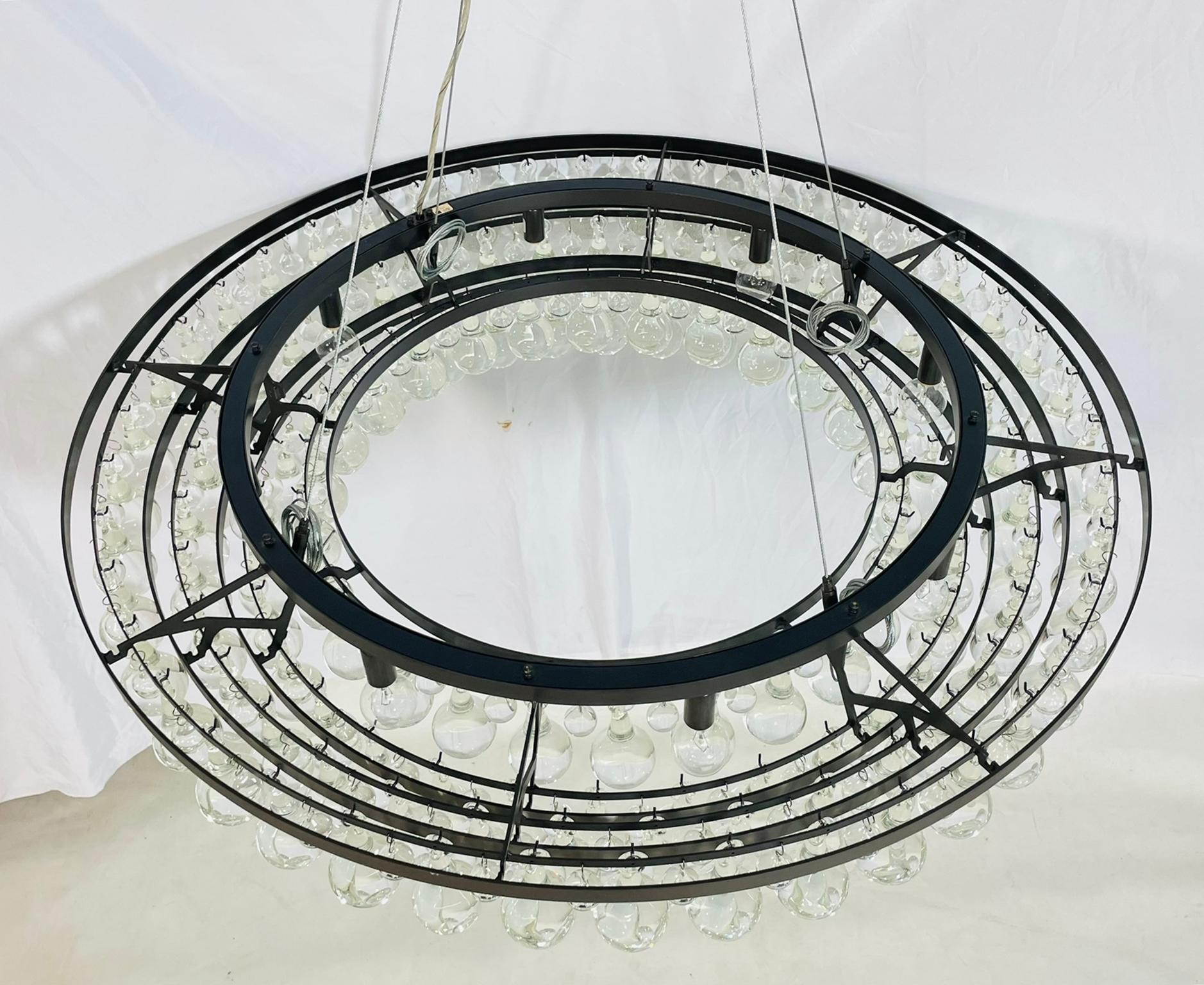 A stunning circular chandelier featuring dozens of hand-blown Murano glass drops suspended from a matte black metal frame. This large-scale contemporary piece blends Italian glass artistry with modern industrial design. The clear glass droplets—each