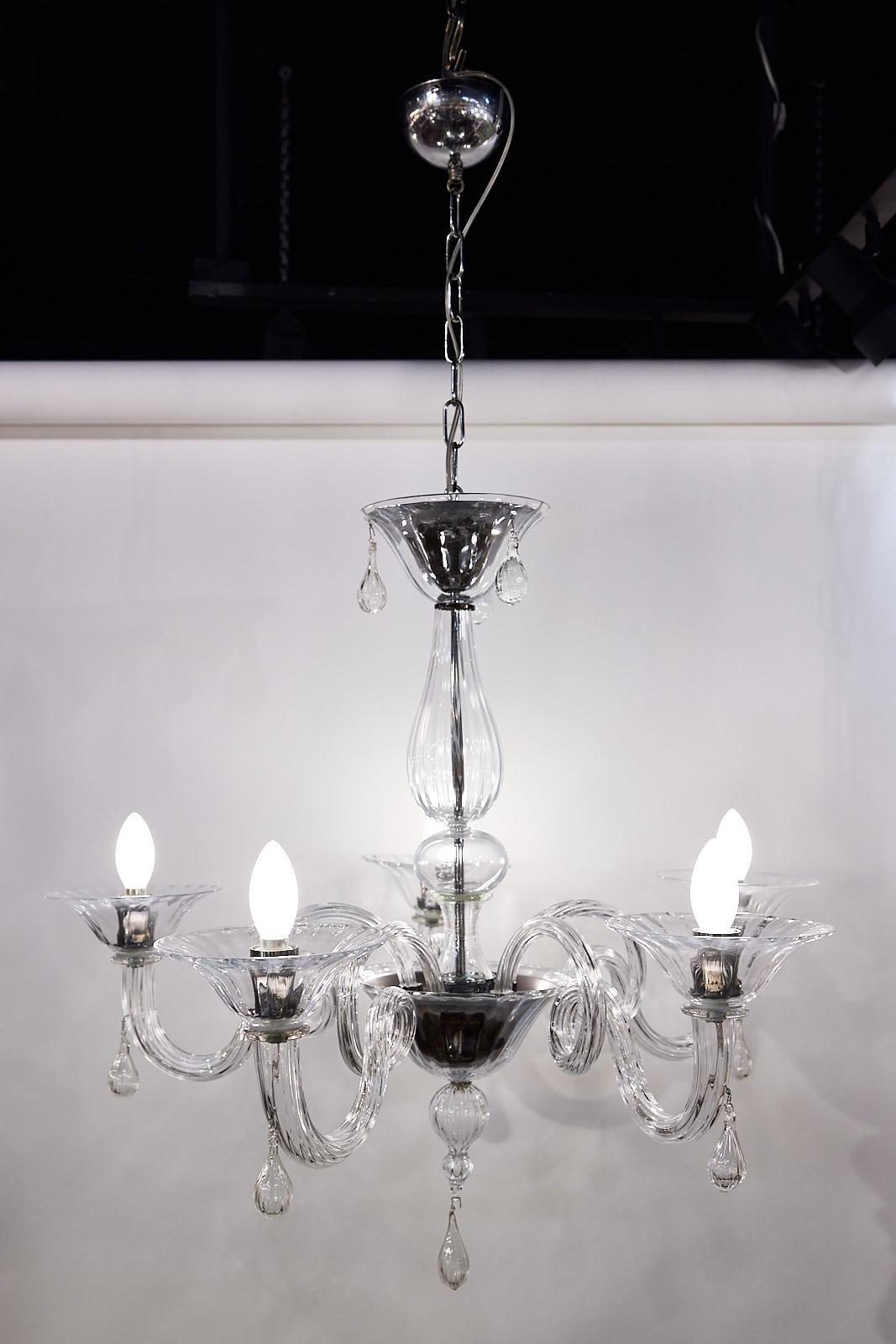 Italian Mid-Century hand-blown Murano glass chandelier having a tiered, central baluster support with five sweeping arms made of twisted, ribbed glass, fluted bobeches, and tear-shaped pedants. The cups and candelabras are chromed adding a layer of
