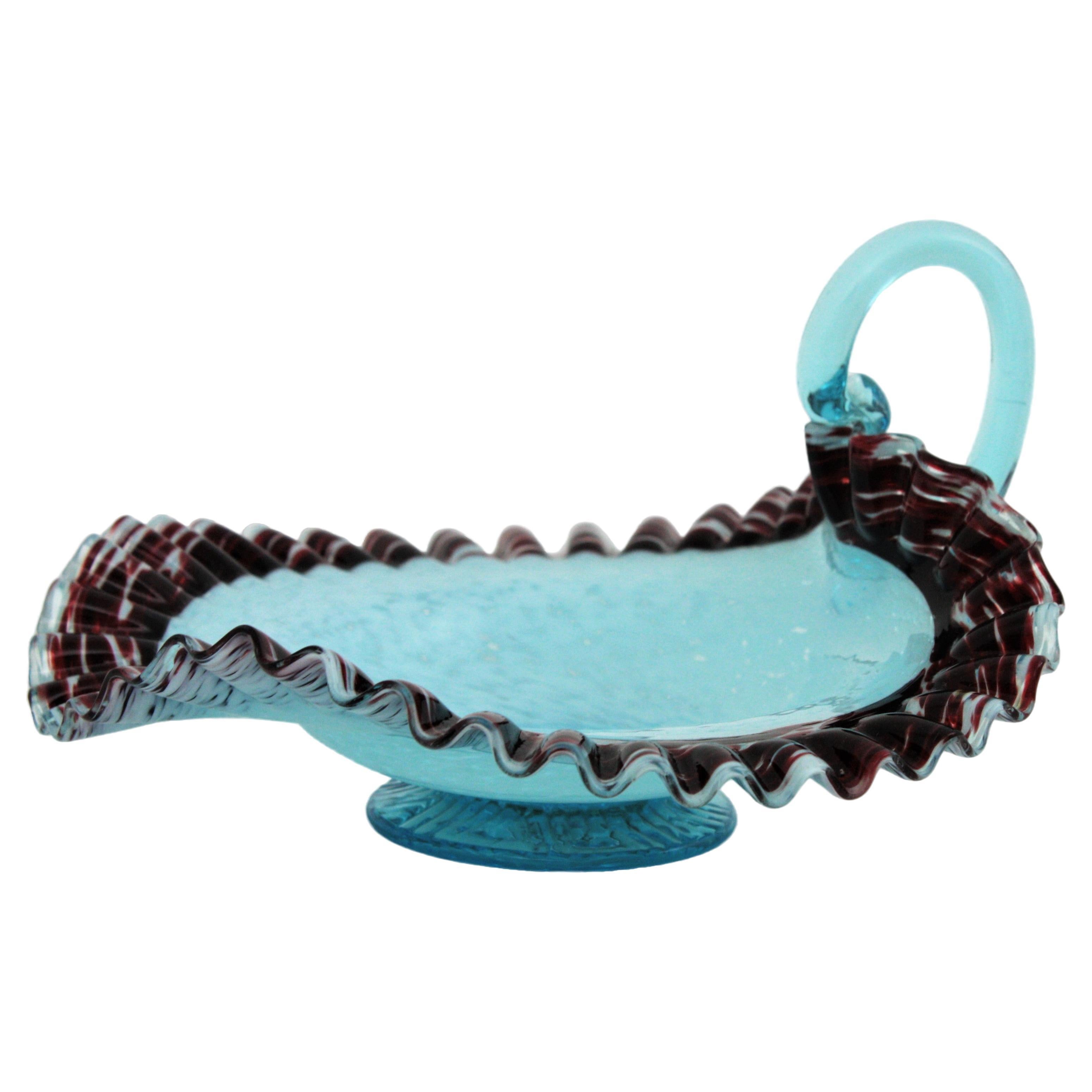 Elegante portacaramelle con piede in vetro di Murano soffiato a mano in stile vittoriano, arricciato e arruffato, di colore blu e granato, Italia, XIX secolo.
Questa squisita coppa di vetro con piede ha uno sfondo con sfumature dal bianco