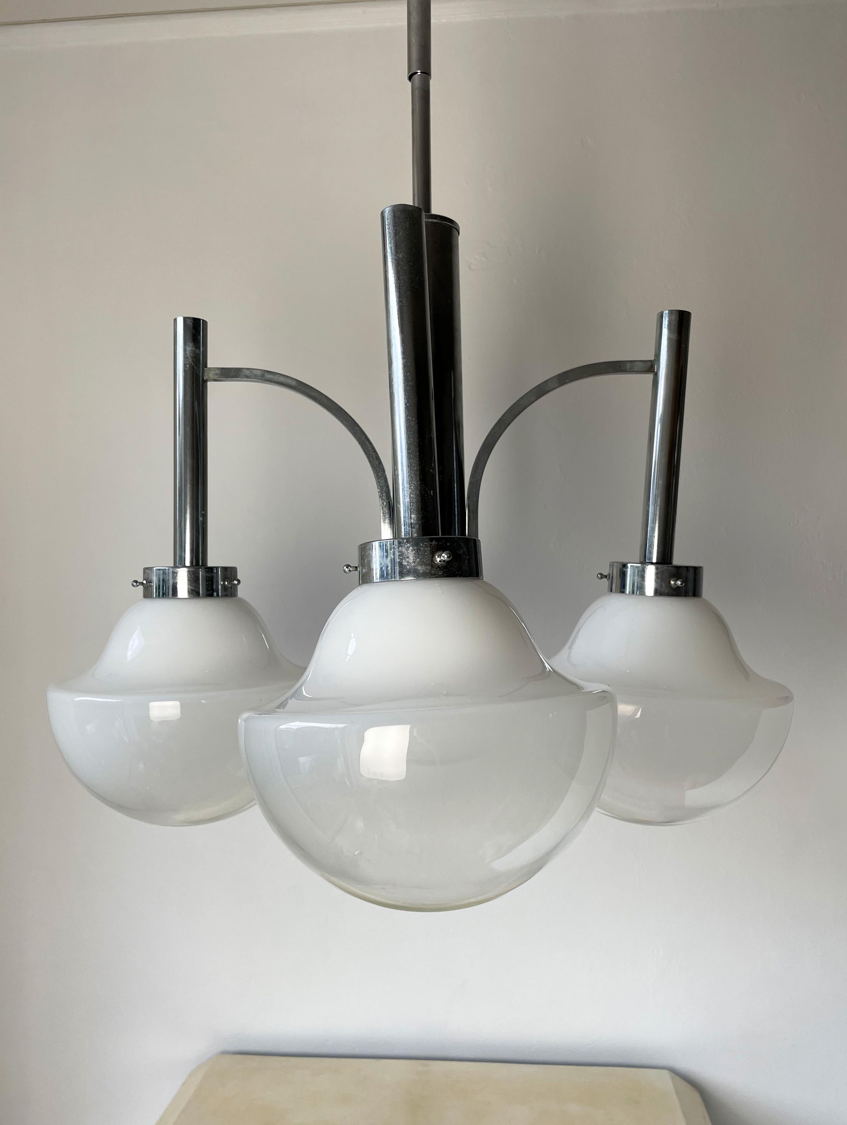 Lampadario scultoreo italiano in stile art deco dell'era atomica, progettato e prodotto nei primi anni '70. Attribuito a Gaetano Sciolari. Quattro splendidi paralumi in vetro di Murano soffiato a bocca di colore bianco latte gradualmente più chiaro