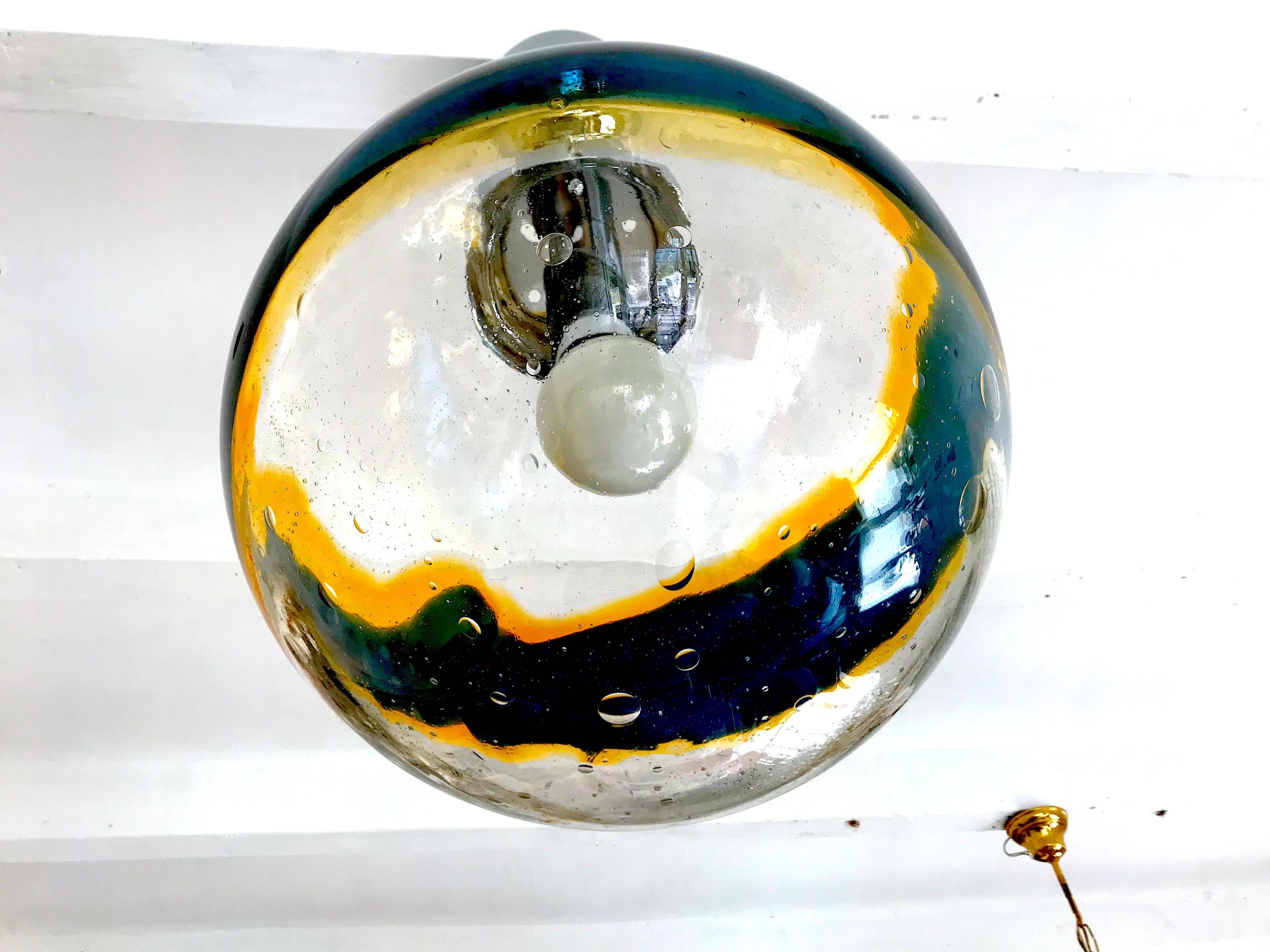 A midcentury handblown Murano globe of clear heavy glass with all-over internal bubbles with an undulating double helix of amber and black, the fixture suspended by a chrome original chain. Measures: 36 cm.
