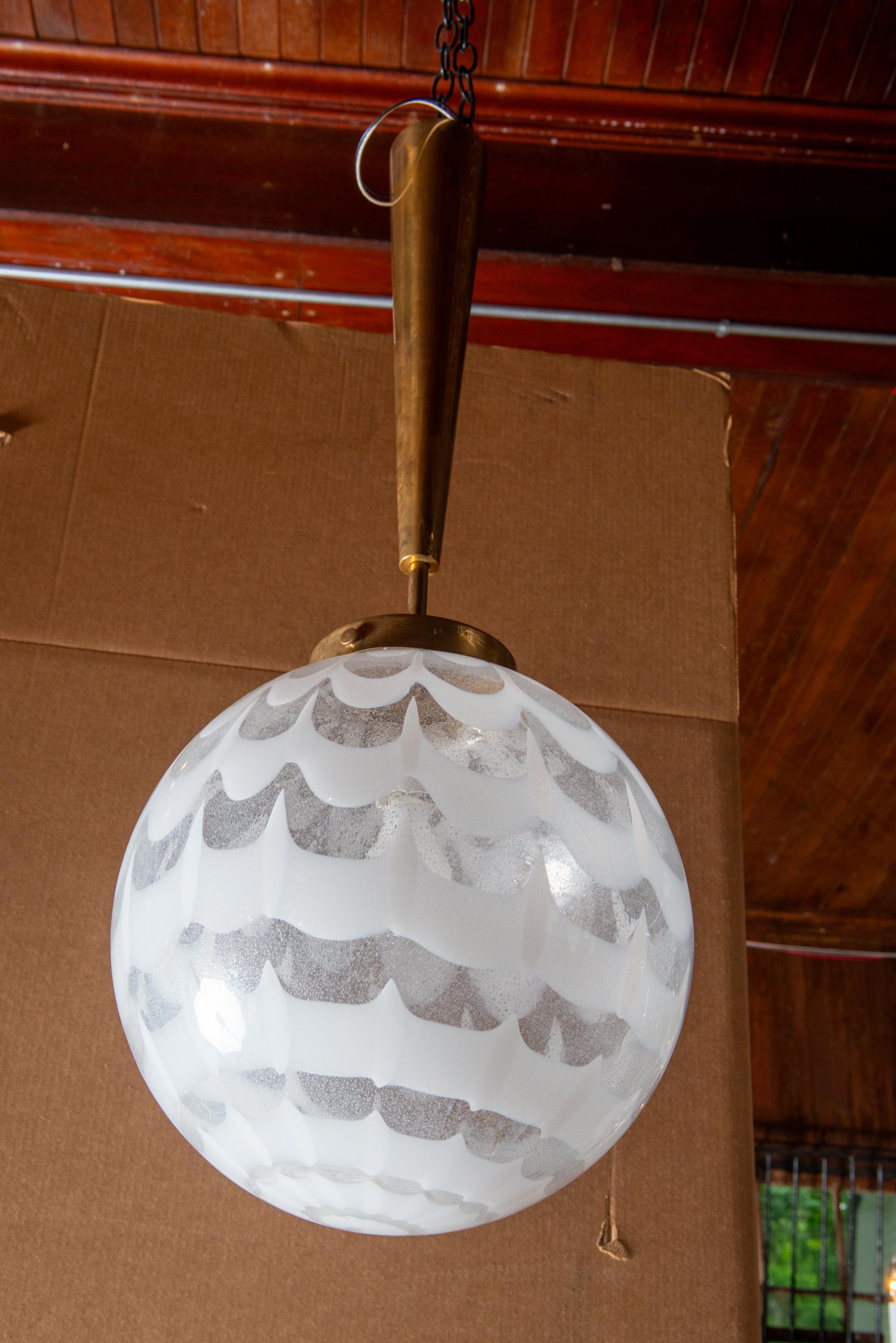 This is a unique hand blown Murano glass globe pendant chandelier. The design of the globe is a white and clear scalloped and spiraled swirl. The brass stem is 19