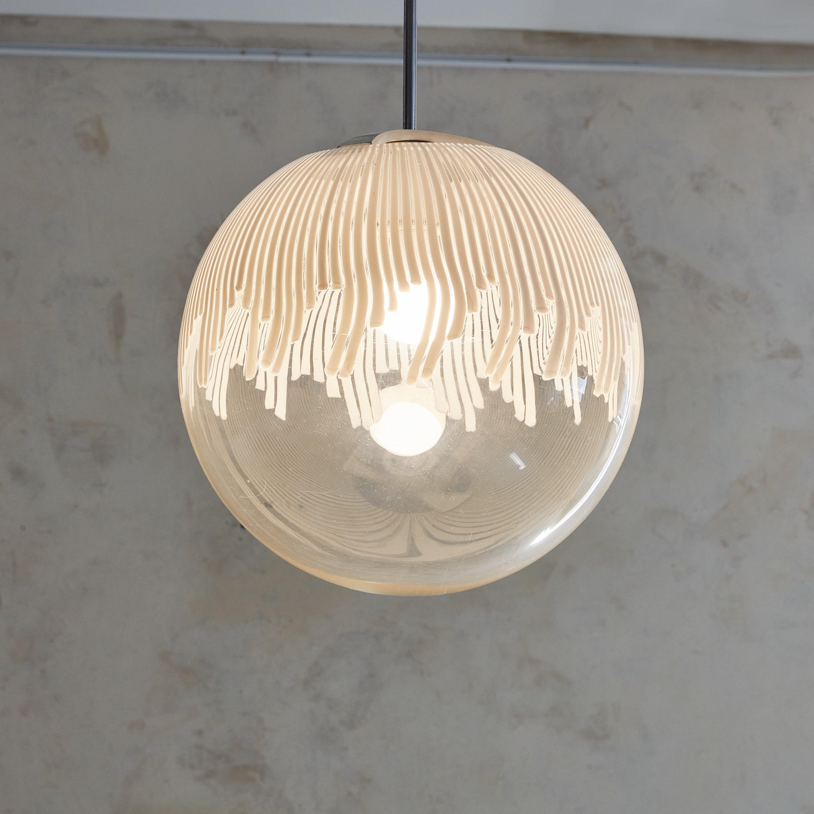 Una squisita lampada a sospensione italiana degli anni '70 con un paralume sferico in vetro di Murano soffiato a mano con un accattivante motivo a strisce bianche. Le strisce delicate e fluide del globo aggiungono un senso di movimento, diffondendo