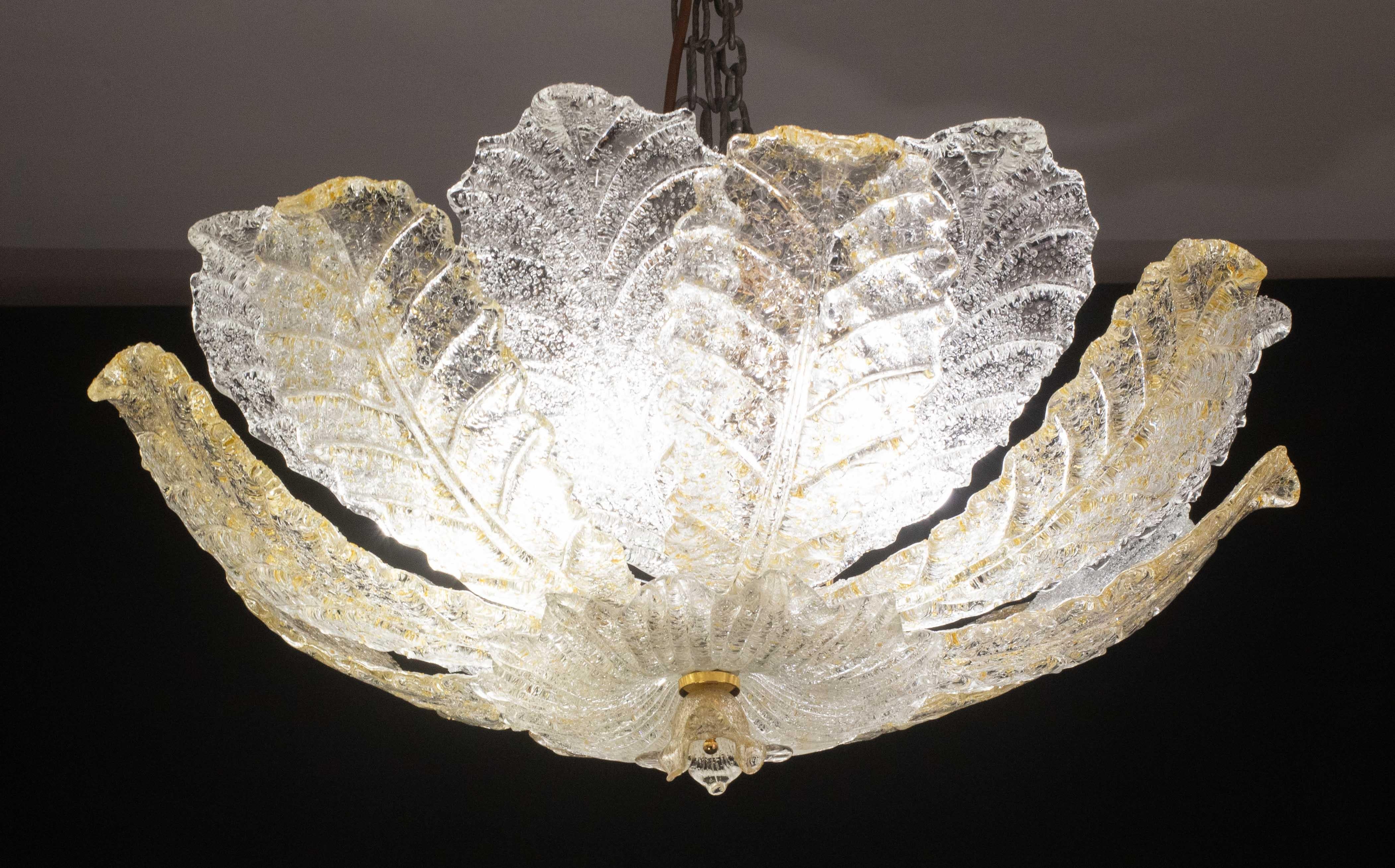 Wunderschöne Deckenlampe aus Murano-Glas mit abwechselnd goldenen und transparenten Glasblättern.
Die Struktur ist vergoldet und darunter braun gestrichen.

Zeitraum: ca. 1970.

Die Leuchte nimmt 6 europäische E15-Standardfassungen auf, die auf