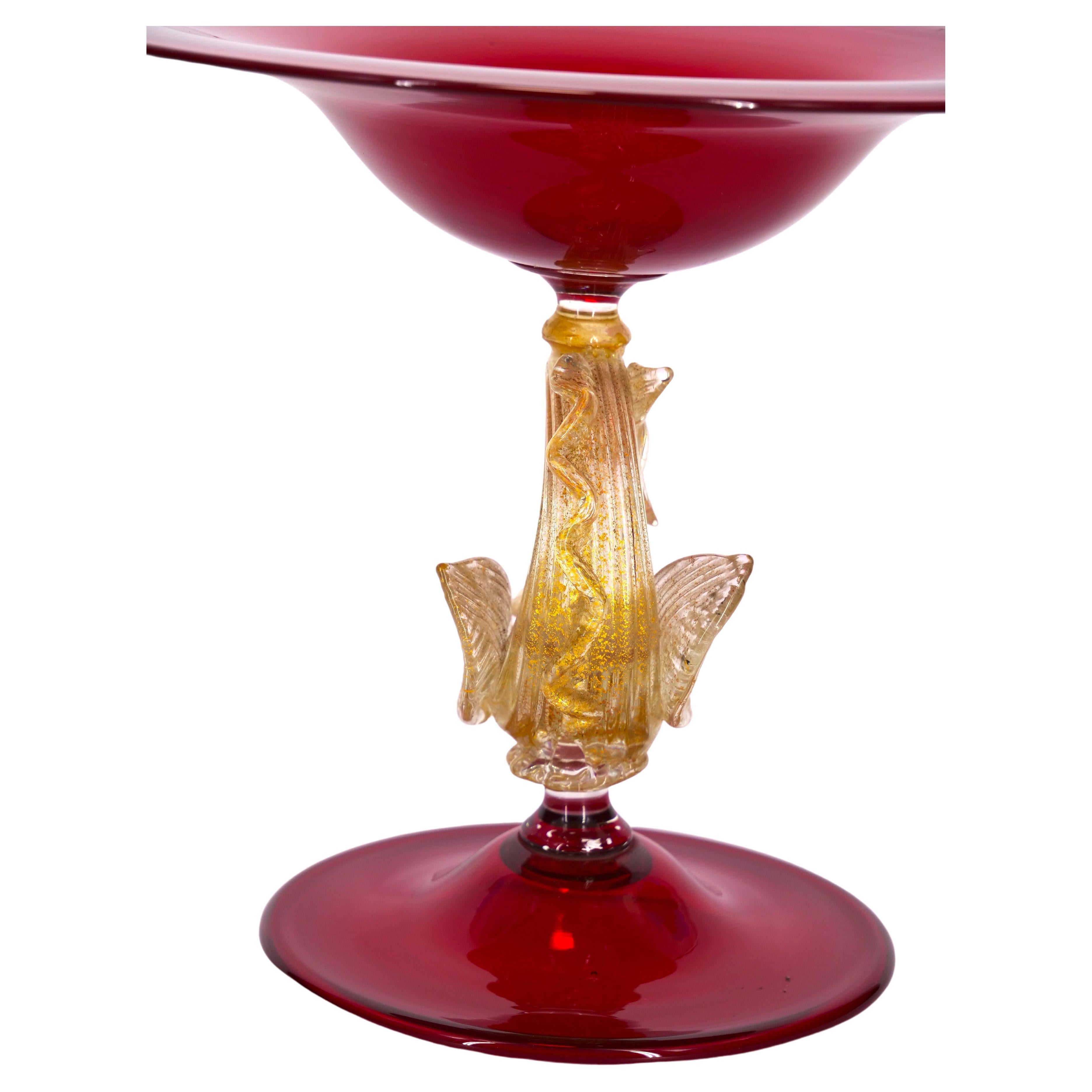 Early 20th century red Murano glass with gold flecks decorative centerpiece / compote. The decorative piece features gold flecks details and resting on gold dolphin resting on a round shape footed base. The centerpiece is in great condition. Maker's