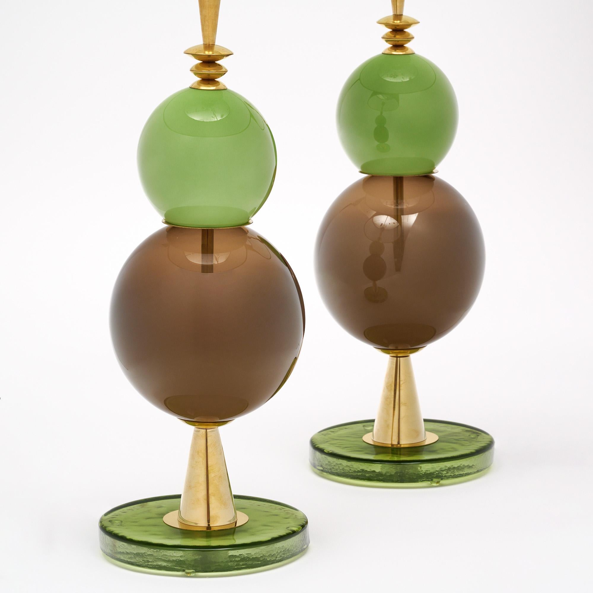 Pareja de lámparas de mesa hechas con elementos de cristal soplado a mano procedentes de Murano, Italia, a las afueras de Venecia. Cada lámpara presenta componentes de cristal únicos en tonos verdes y grises sobre una estructura de latón. Nos