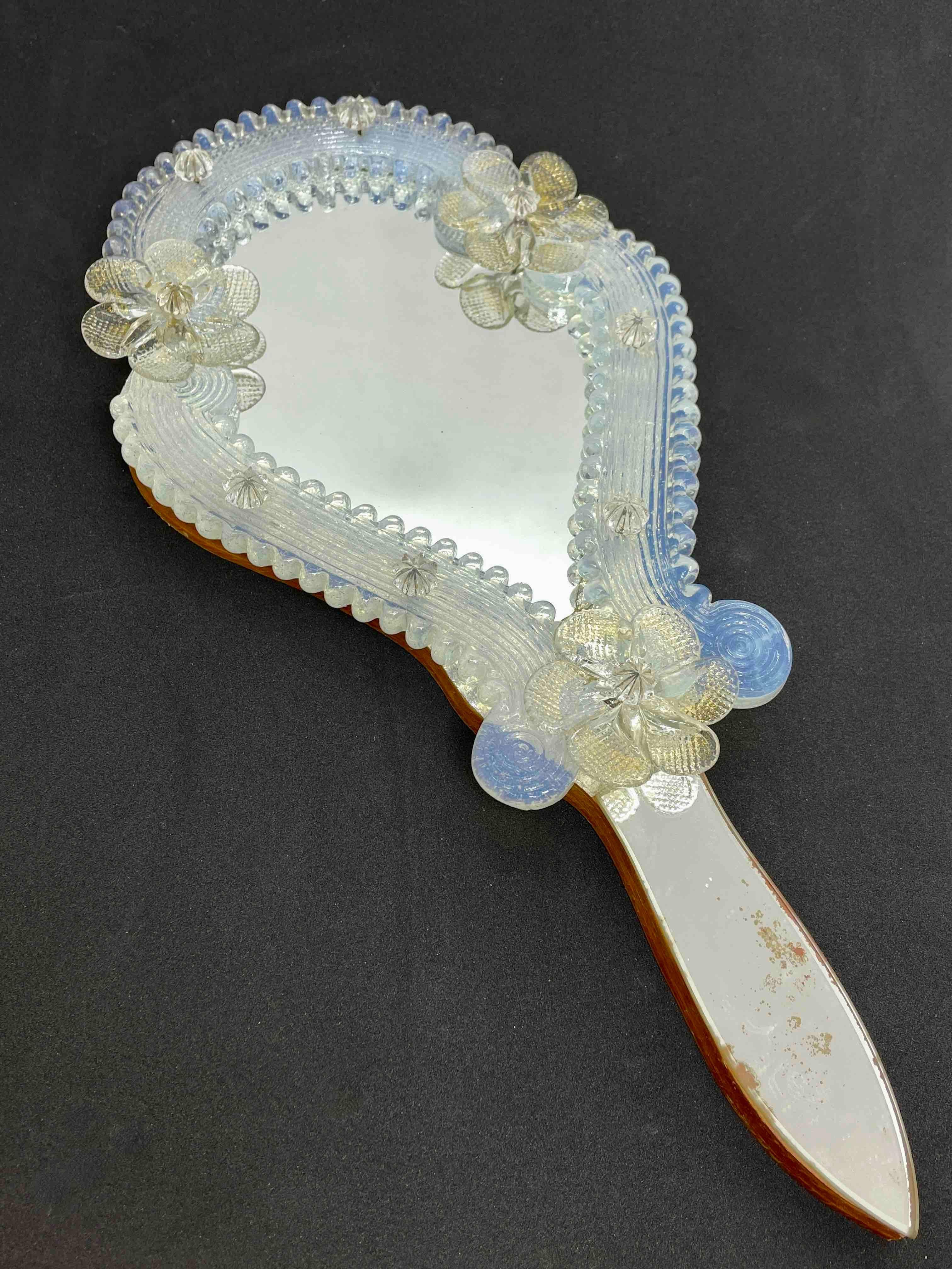 A gorgeous Murano glass vanity mirror surrounded with handmade gold flake glass flowers and iridescent glass ornaments. Can be used as a handheld or a wall mirror. With minor signs of wear as expected with age and use. A nice addition to any girls