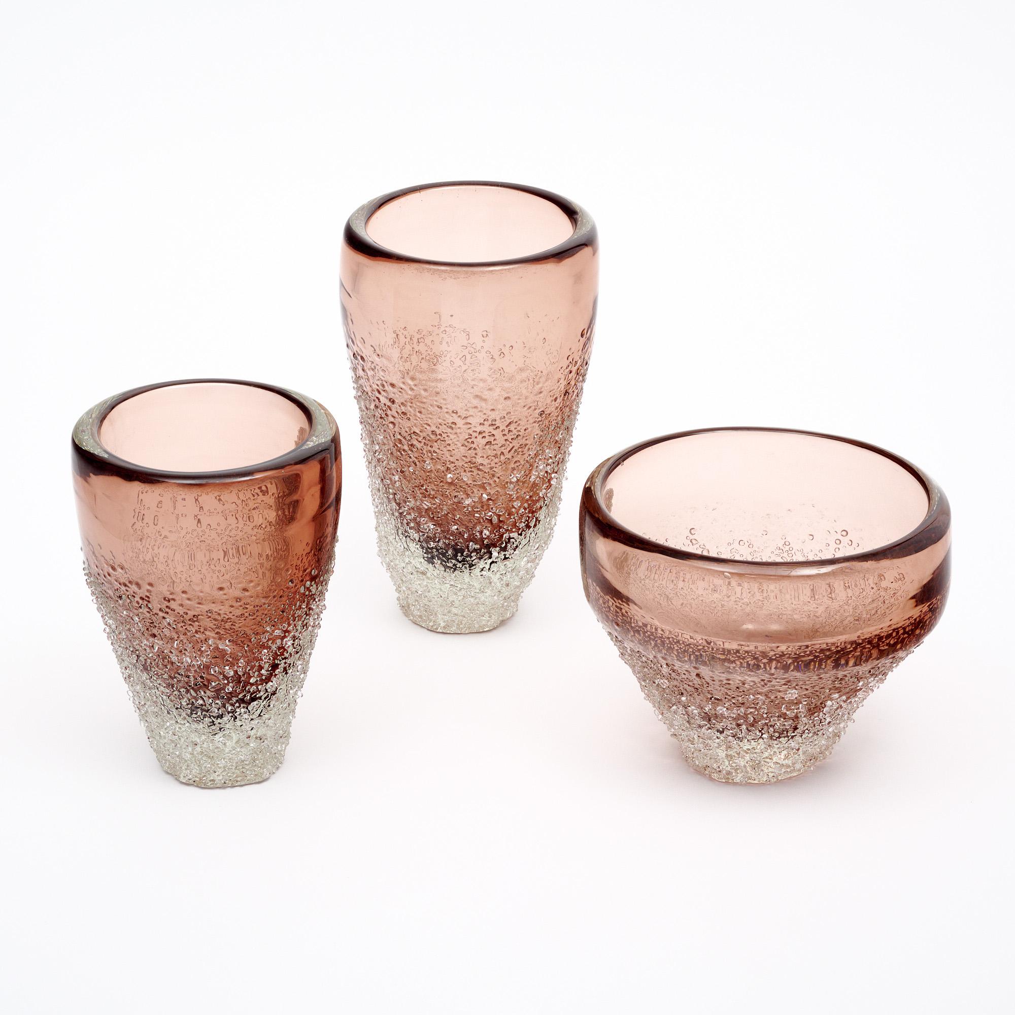 Set of Murano glass vases from the island of Murano outside of Venice, Italy. The set of three is hand-blown in a beautiful mauve color. Each showcases several striking glass techniques. While the glass is still in fusion, each vase was rolled in