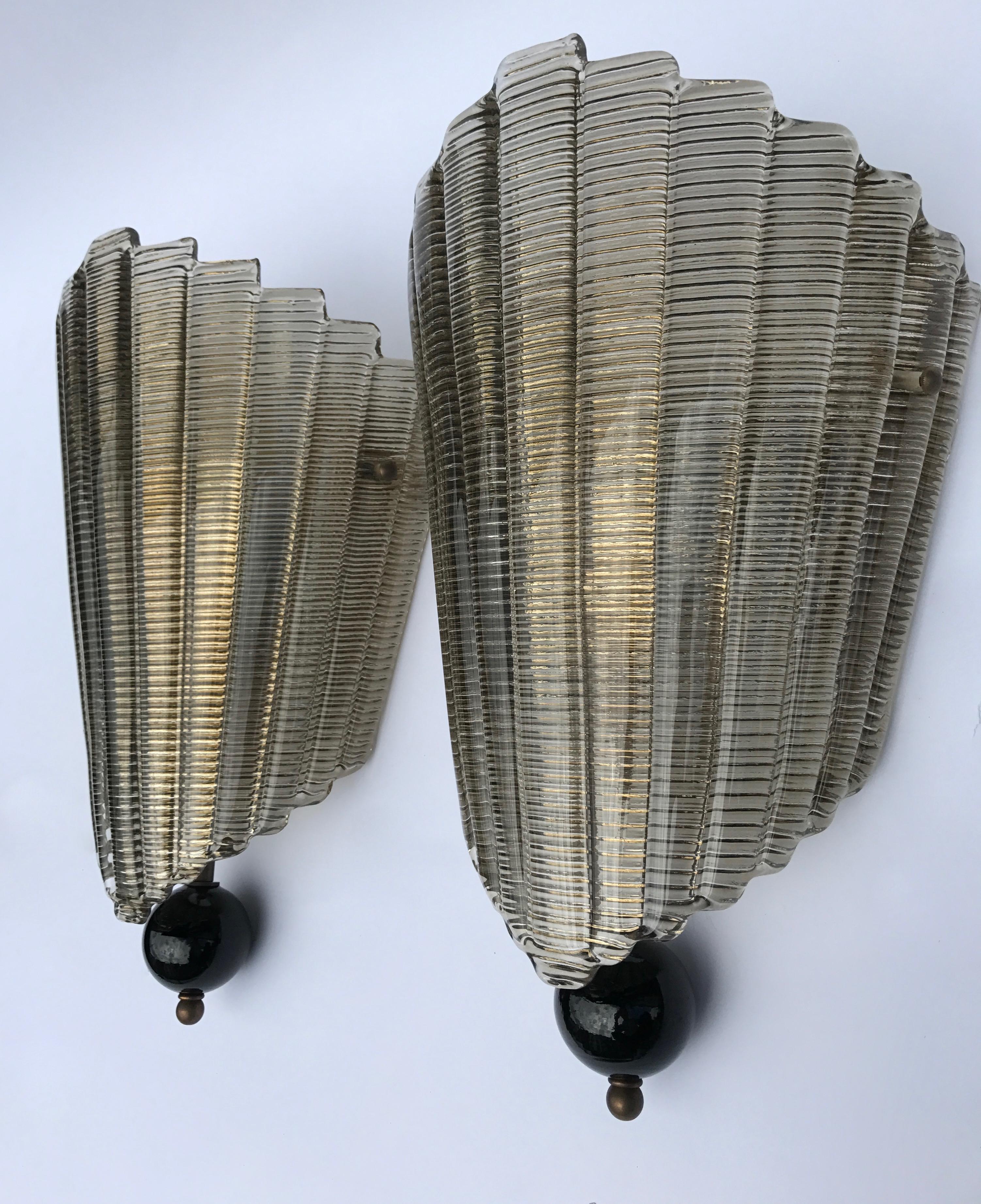 Le verre de Murano en forme d'éventail est simplement fixé par deux vis en laiton au support mural pour former cette applique de style Art déco, belle et efficace.
Le verre présente des gravures qui lui donnent un aspect doré lorsque la lumière se