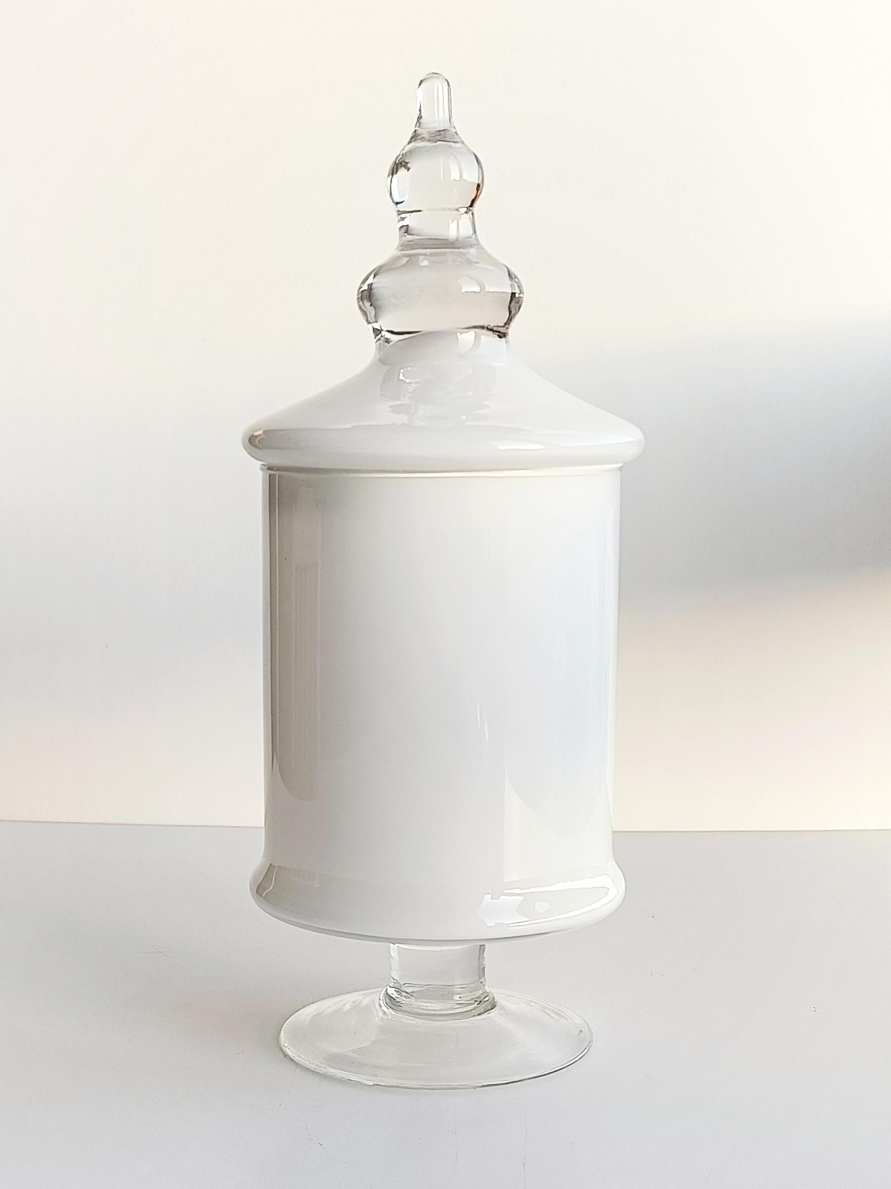 Elegant hand-blown Murano glass bombon jar. Delicately crafted, this jar showcases a combination of a thin layer of clear glass lined by an equally thin white casing. The lid handle and base are made from clear glass. 

Standing at a height of 33cm
