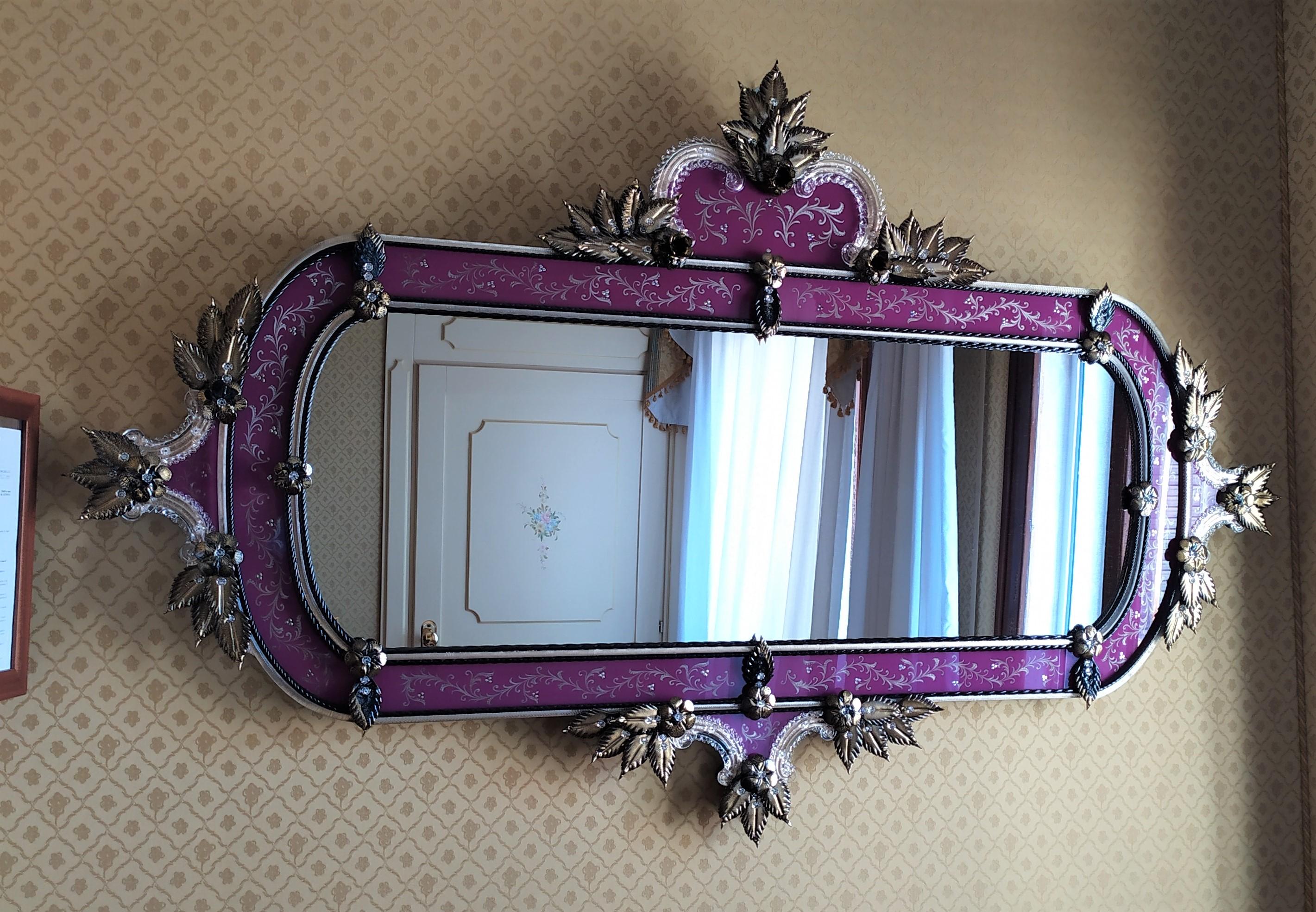 Miroir horizontal de style vénitien, revisité en couleurs.
Miroir en verre de Murano, avec cadre gravé à la main réalisé selon les anciennes traditions muranaises, de couleur violette, avec des roseaux, des feuilles et des fleurs de couleur or