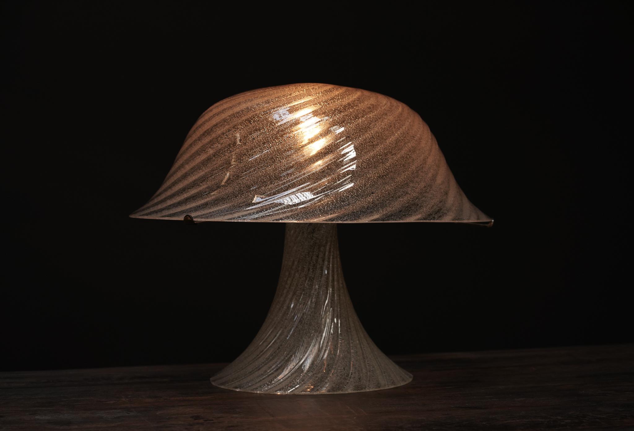 A timeless expression of Italian craftsmanship, this Murano glass table lamp features a sleek mushroom silhouette in crystal-clear glass. Its sculptural form and soft, diffused glow make it a striking yet versatile addition to any space, blending