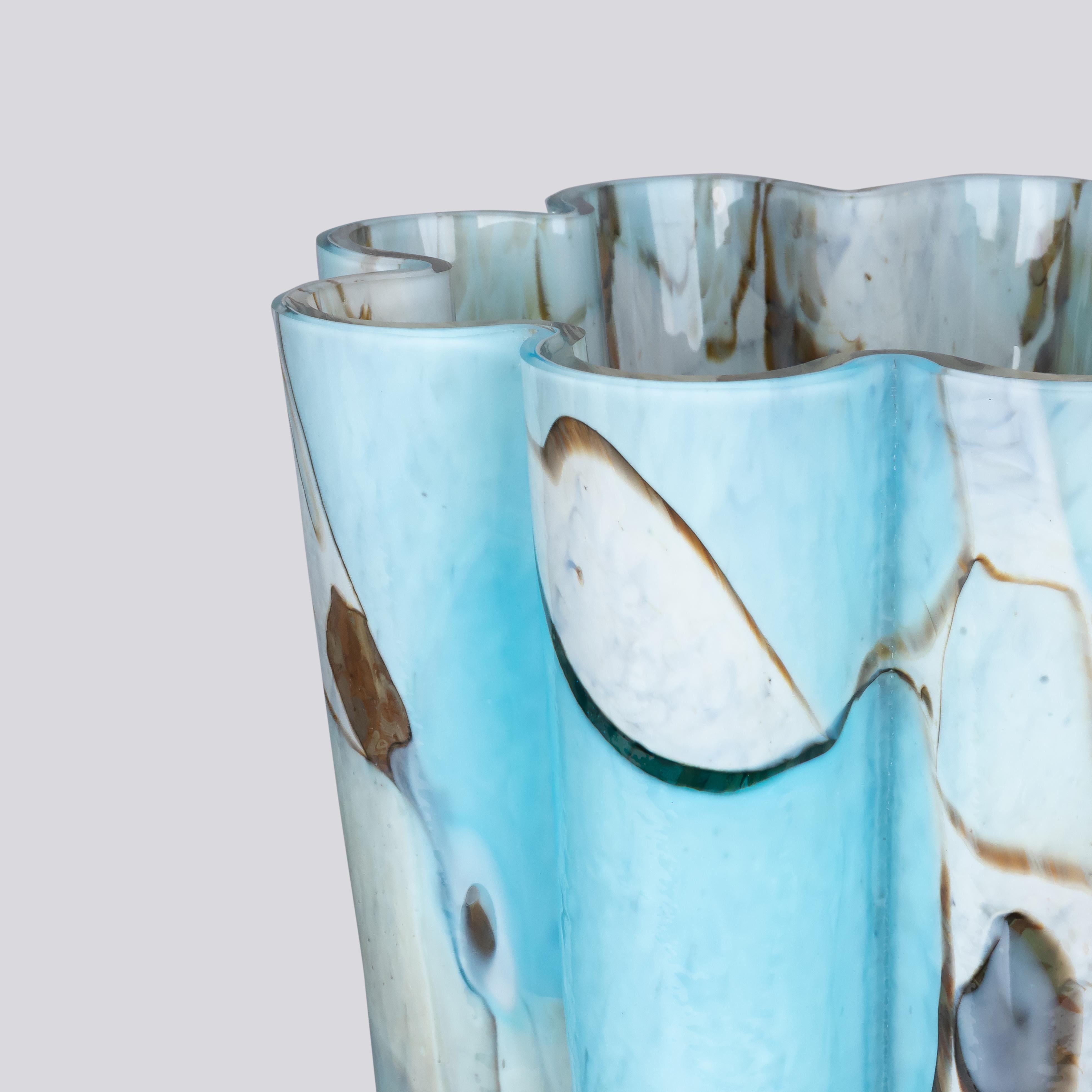 Crafted in the shape of a blooming flower, the Bucket vase features a captivating fusion of colors, with mesmerizing aquamarine shards of glass gracefully melted onto an ivory glass base. The result is a breathtaking display of serene blue hues,