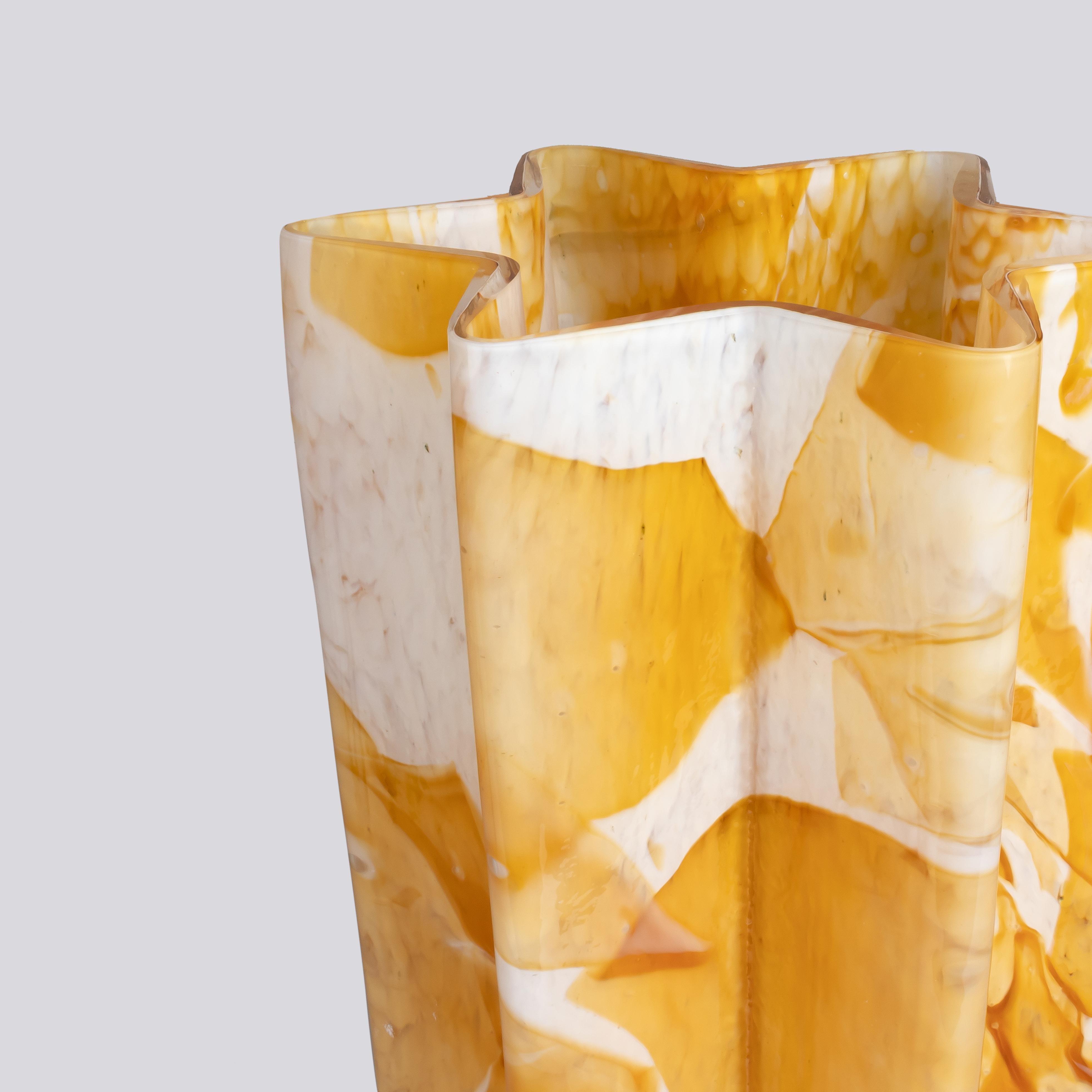 This stunning piece is shaped like a star, showcasing a captivating fusion of deep amber shards of glass melted onto an ivory glass base.The Karkadè Bucket vase is meticulously mouth-blown and hand-finished by skilled artisans from Murano, Italy,