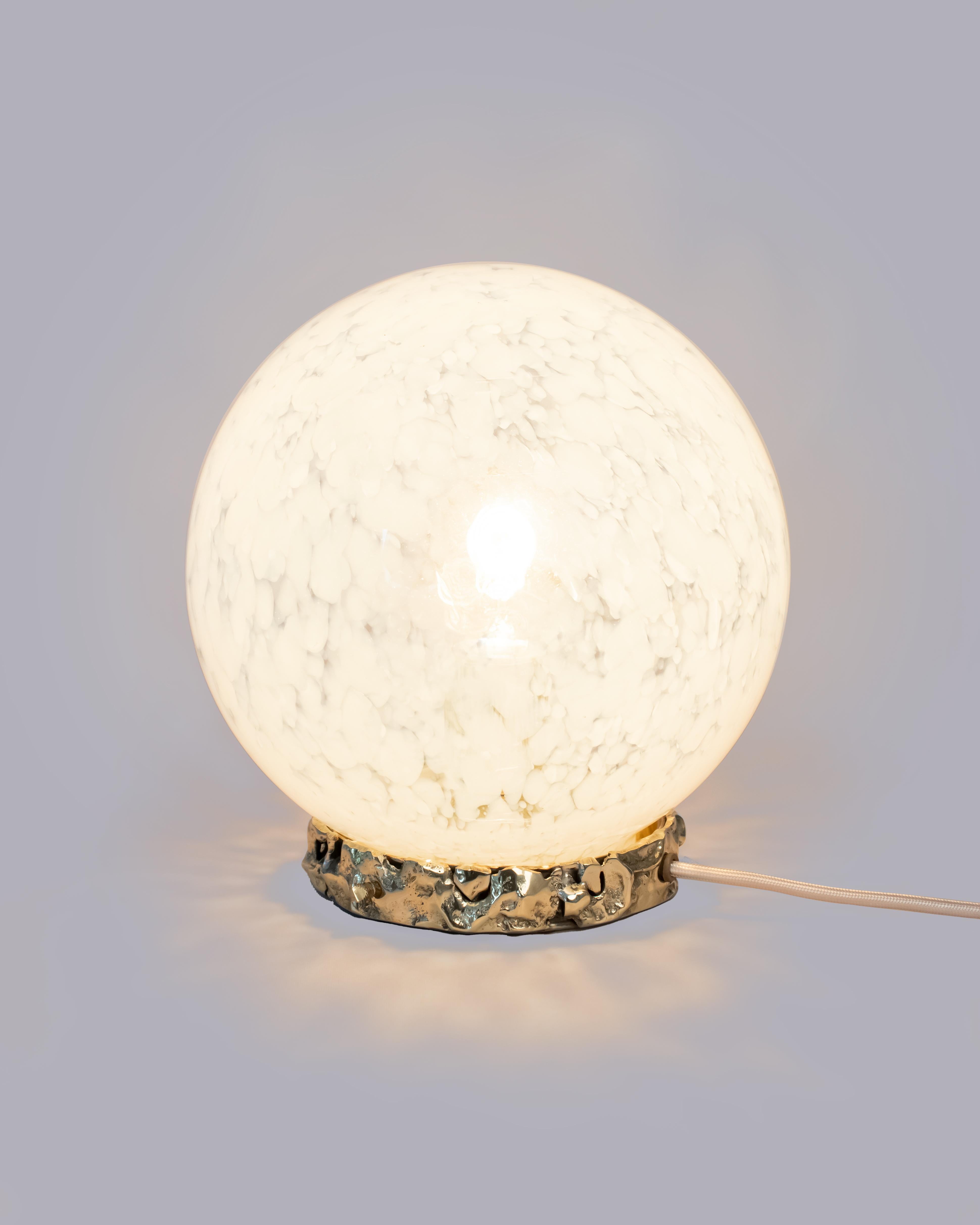 Te presentamos la Lámpara Corona, una pieza luminosa perfecta para realzar tu salón, dormitorio o cualquier espacio que desees impregnar con un toque de lujo y elegancia. Su base es de latón fundido, con una superficie irregular y de textura