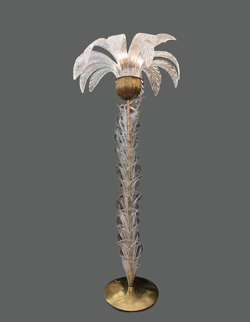 Murano glass palm tree floor lamp with clear glass leaves, brass base and fittings, three bulbs. The floor lamp is also a sculpture that reproduces with the clear hand blown Murano glass pieces the trunk and the leaves of a palm.


