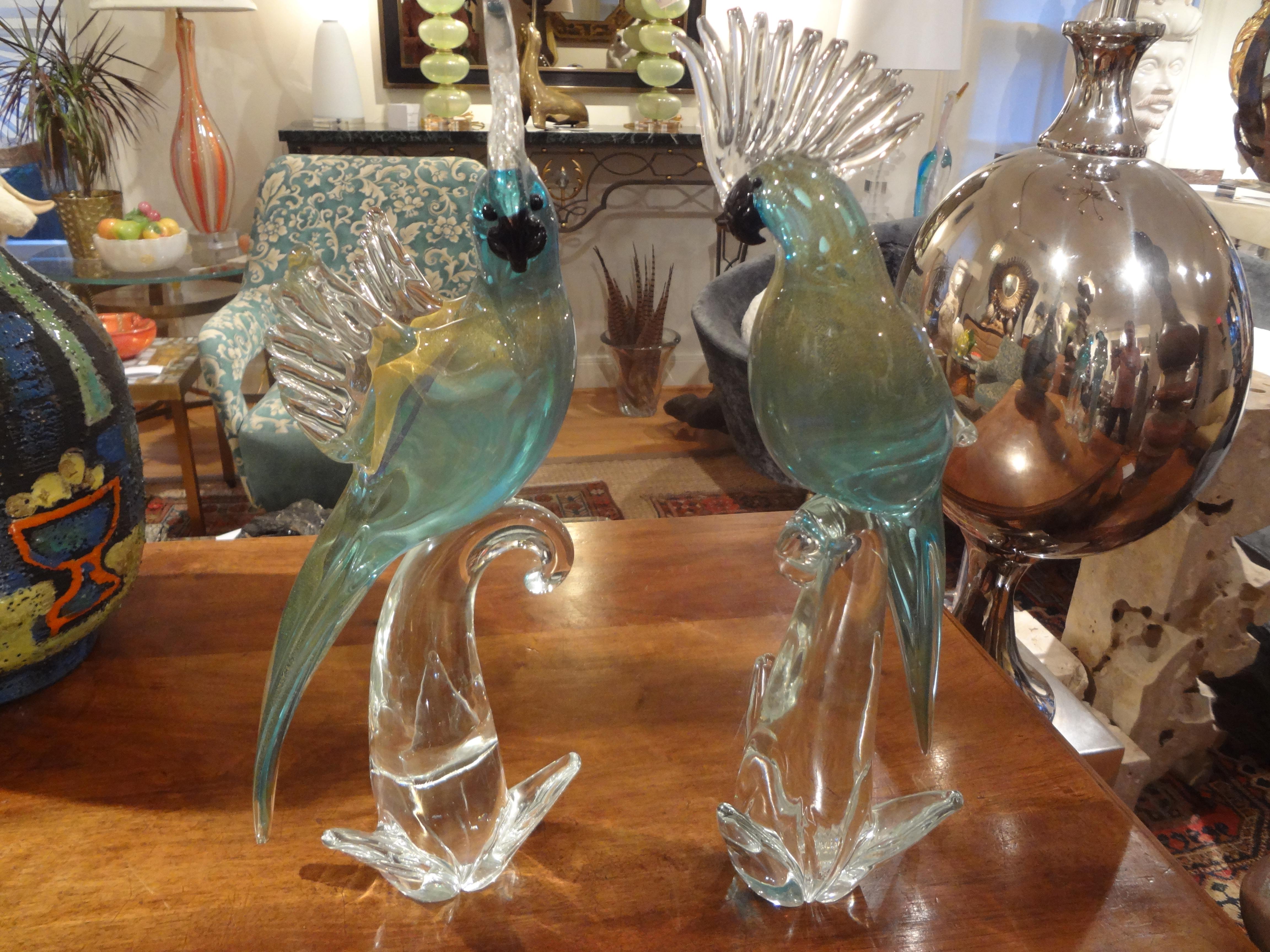 A gorgeous pair of blown Murano glass parrot sculptures. This pair of Murano parrots was executed in a fabulous blue glass with gold inclusions throughout. This pair of midcentury parrots rests on clear glass bases and one retains the original