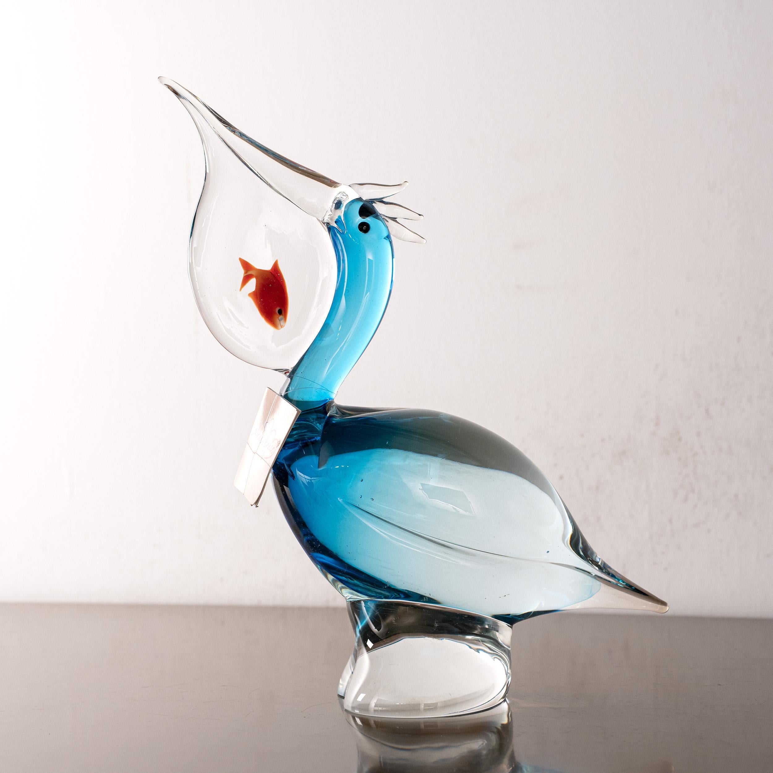 A striking hand-blown Murano glass pelican in vibrant turquoise, holding a shimmering goldfish in its beak. A whimsical and original 1980s decorative sculpture from Italy.

Dimensions: L 25 cm x H 31 cm x D 25 cm ( L 9.8