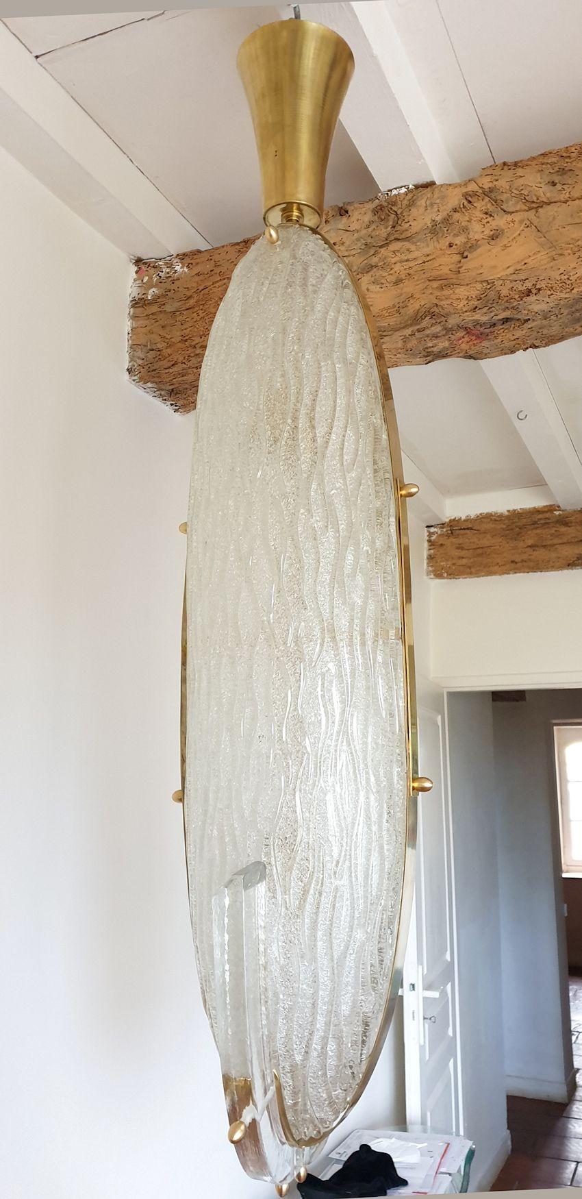 Mid-Century Modern pendant ceiling light, or large lantern, with a long oval shape, in clear Murano glass and brass ornements, Barovier & Toso style Italy 1970s.
The vintage chandelier is made of translucent, thick, clear Murano glass with a kind of