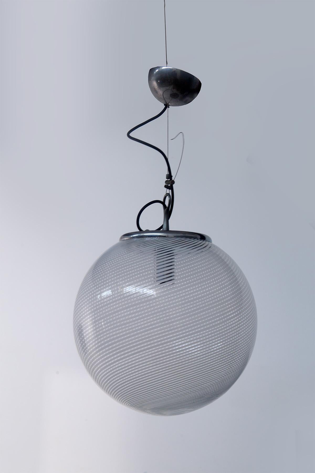 Cette superbe lampe suspendue, fabriquée dans les années 1970 par Venini, incarne l'excellence de l'art du verre de Murano. Son design est pur et essentiel - un globe de verre parfait qui incarne l'élégance et le raffinement typiques de la marque