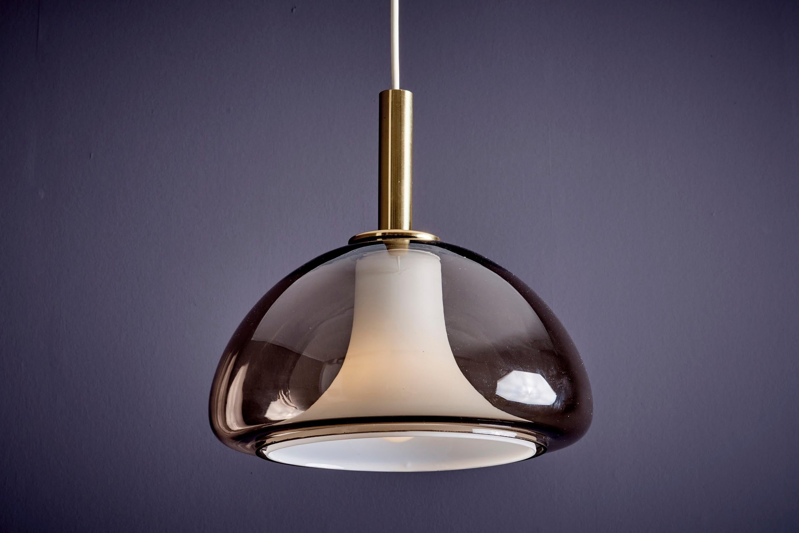 legante lampada a sospensione italiana di metà secolo. Il design è caratterizzato da un paralume esterno in vetro di Murano fumé e da un diffusore interno opalino che proietta una luce calda e diffusa. Rifinito con uno stelo in ottone, questo pezzo