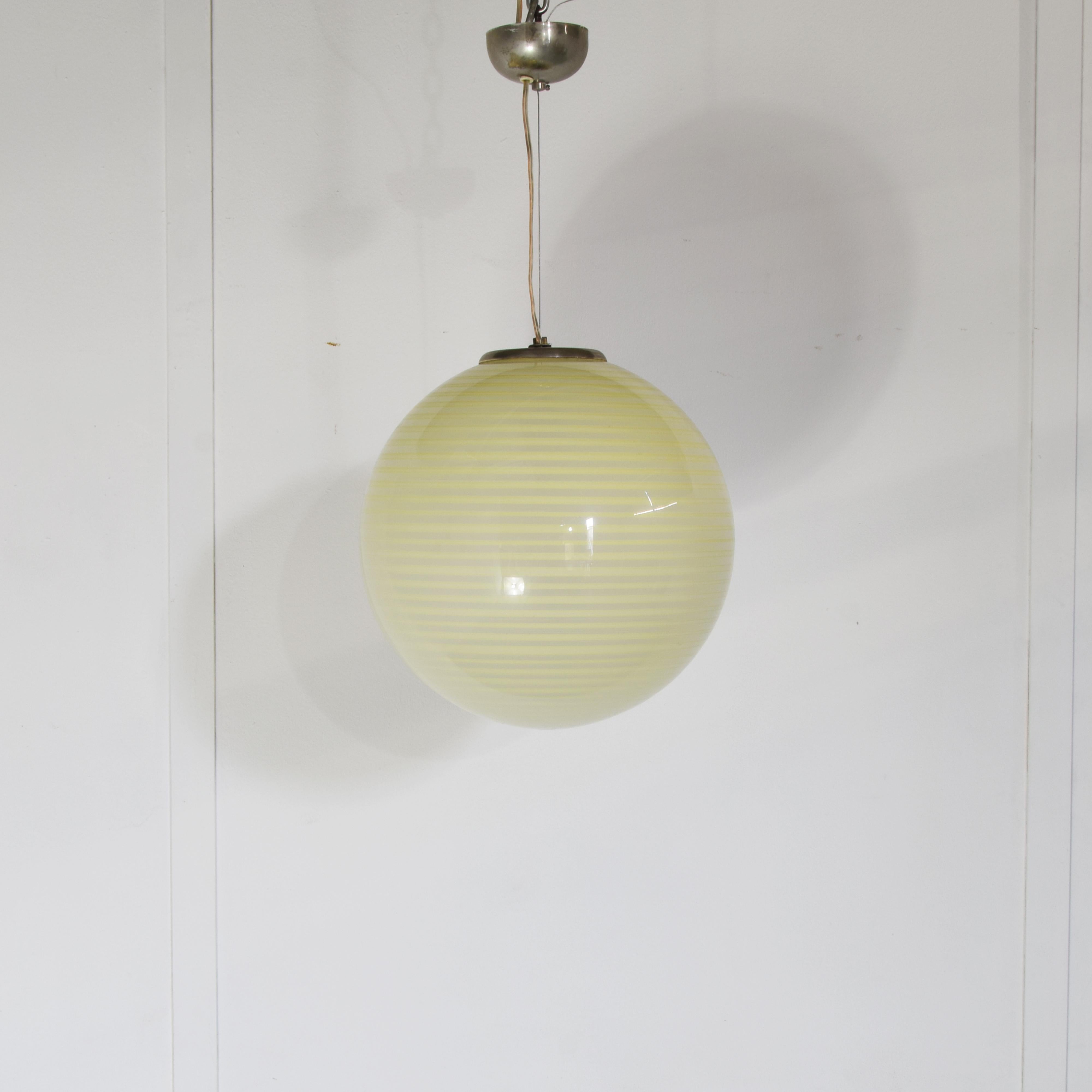 This pendant lamp Vennini att. is distinguished by its elegant spherical shape and refined craftsmanship in Murano glass, executed according to the ancient techniques of Venetian master glassmakers. The glass is embellished with a twisted filigree,