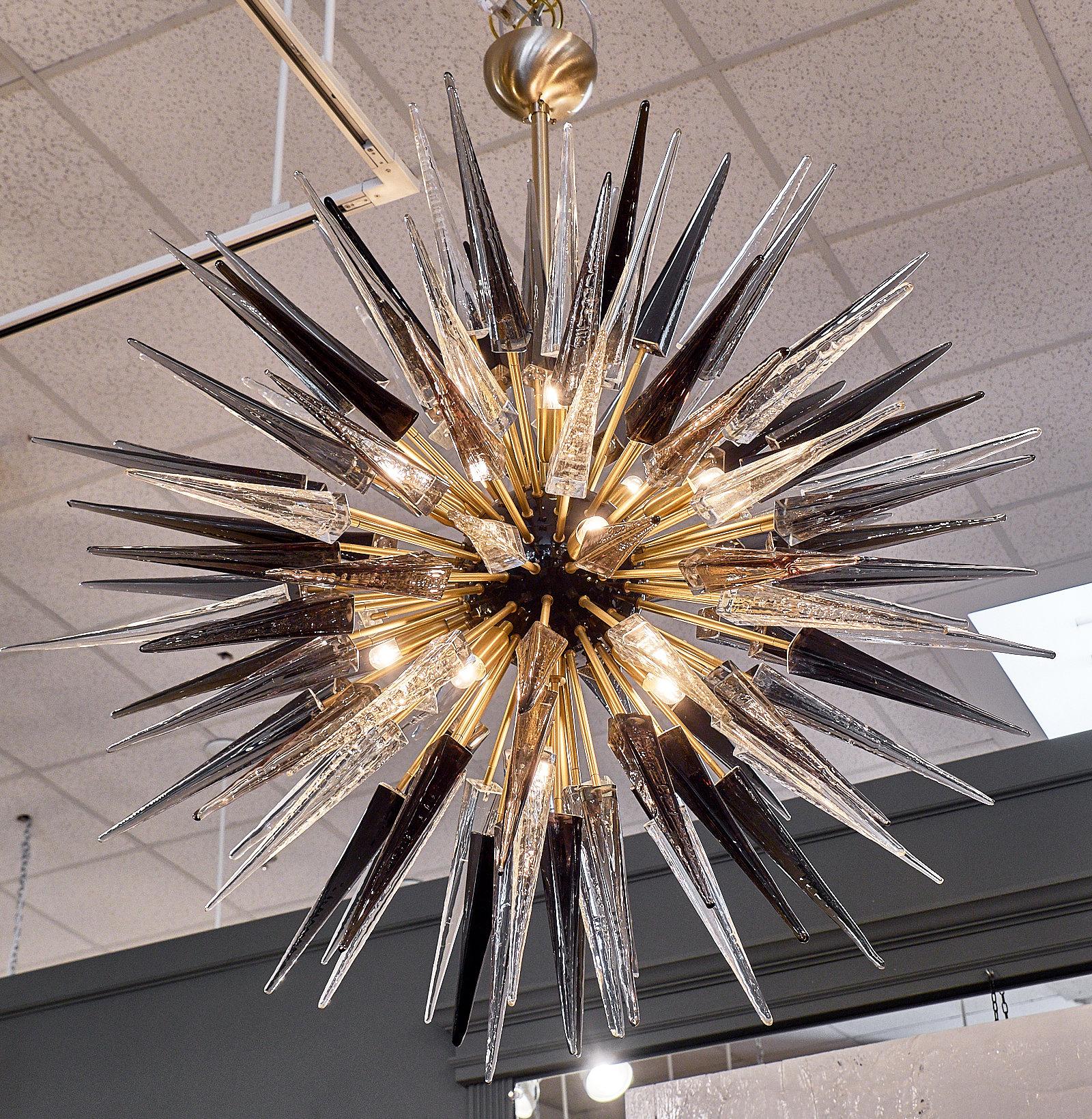Lampadario a prisma sputnik in vetro di Murano. Questo apparecchio presenta numerosi prismi soffiati a mano di vari colori (nero, grigio, trasparente) montati su una struttura in ottone dorato. Questo spettacolare lampadario ha un impatto decorativo