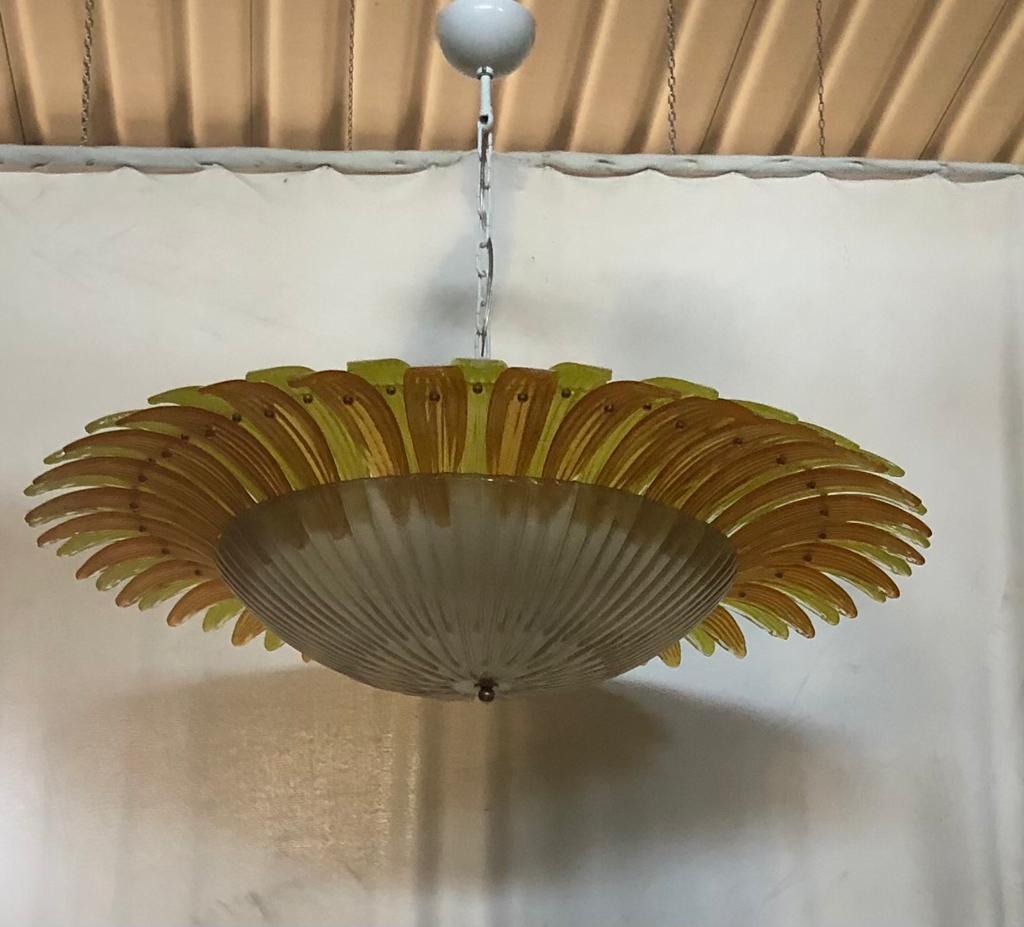 Triomphe des feuilles de Murano jaunes pour un lustre unique en son genre, tel un énorme tournesol que vous aurez au-dessus de votre tête.

Le lustre ou grand plafonnier, est composé d'une structure ronde en fer à laquelle a été fixée une série de