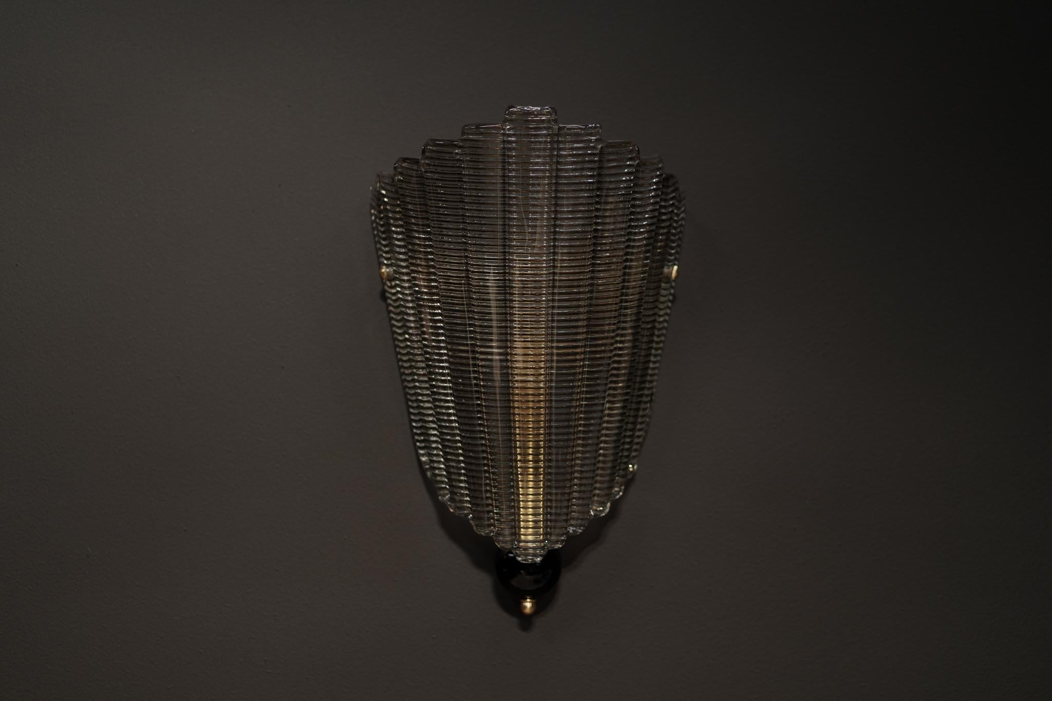 Este candelabro contemporáneo de cristal de Murano soplado a mano presenta una pantalla de cristal texturizado, combinada con latón refinado y un acento de esfera negra. Escultural y moderno, añade un brillo sofisticado y artesanía italiana a