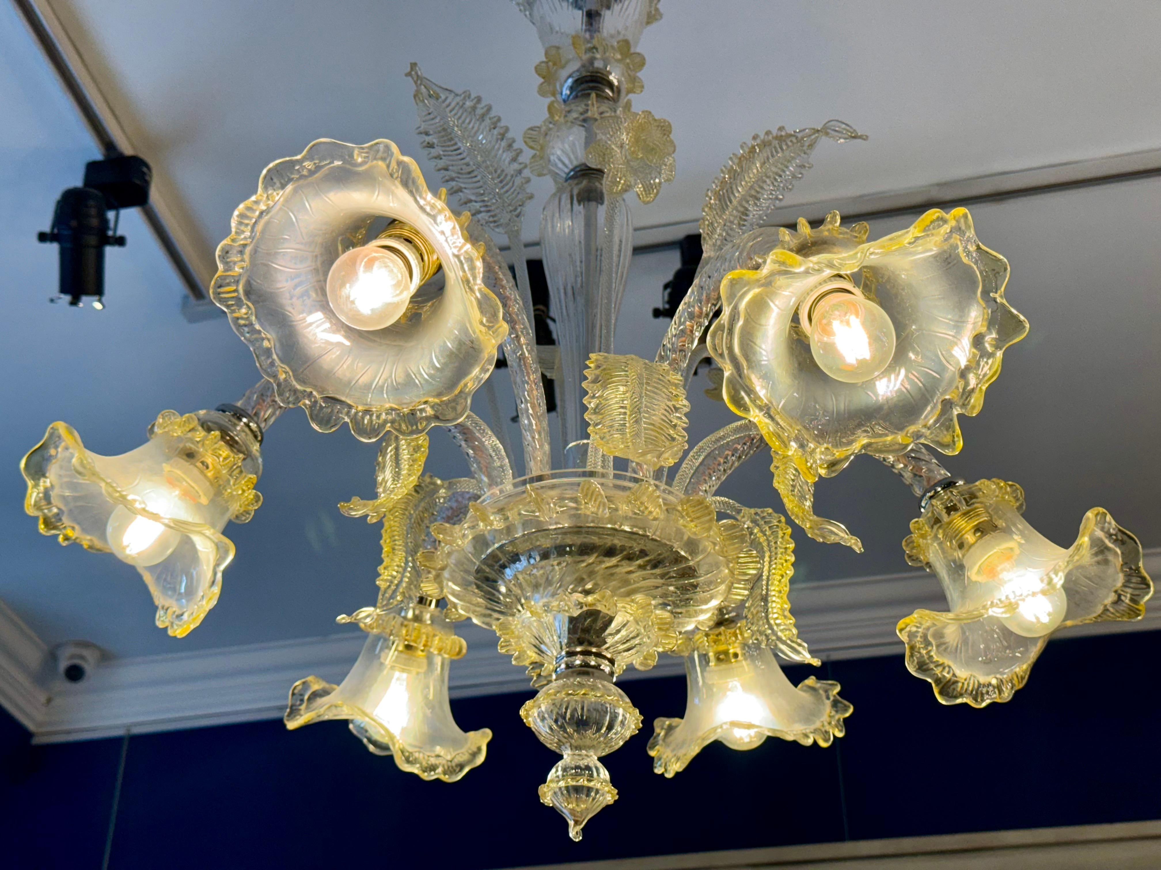 This stunning Murano glass chandelier from the 1960s features a striking six-arm design in a radiant palette of yellow and white. Handcrafted with meticulous attention to detail, each arm gracefully curves and flares, creating a luminous effect that
