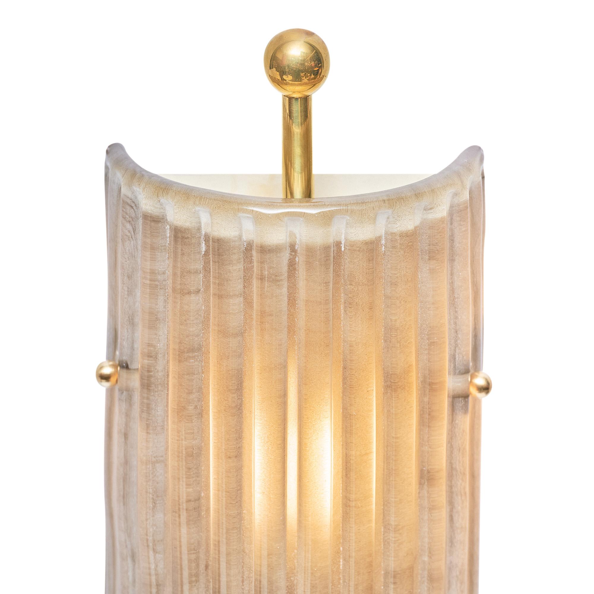 Pair of sconces in the Art Deco style made of ribbed Murano glass with a brass structure. The structure features brass finials at the top and bottom for a timeless yet sleek aesthetic. The glass is a beautiful smoked and frosted tone for a subtle