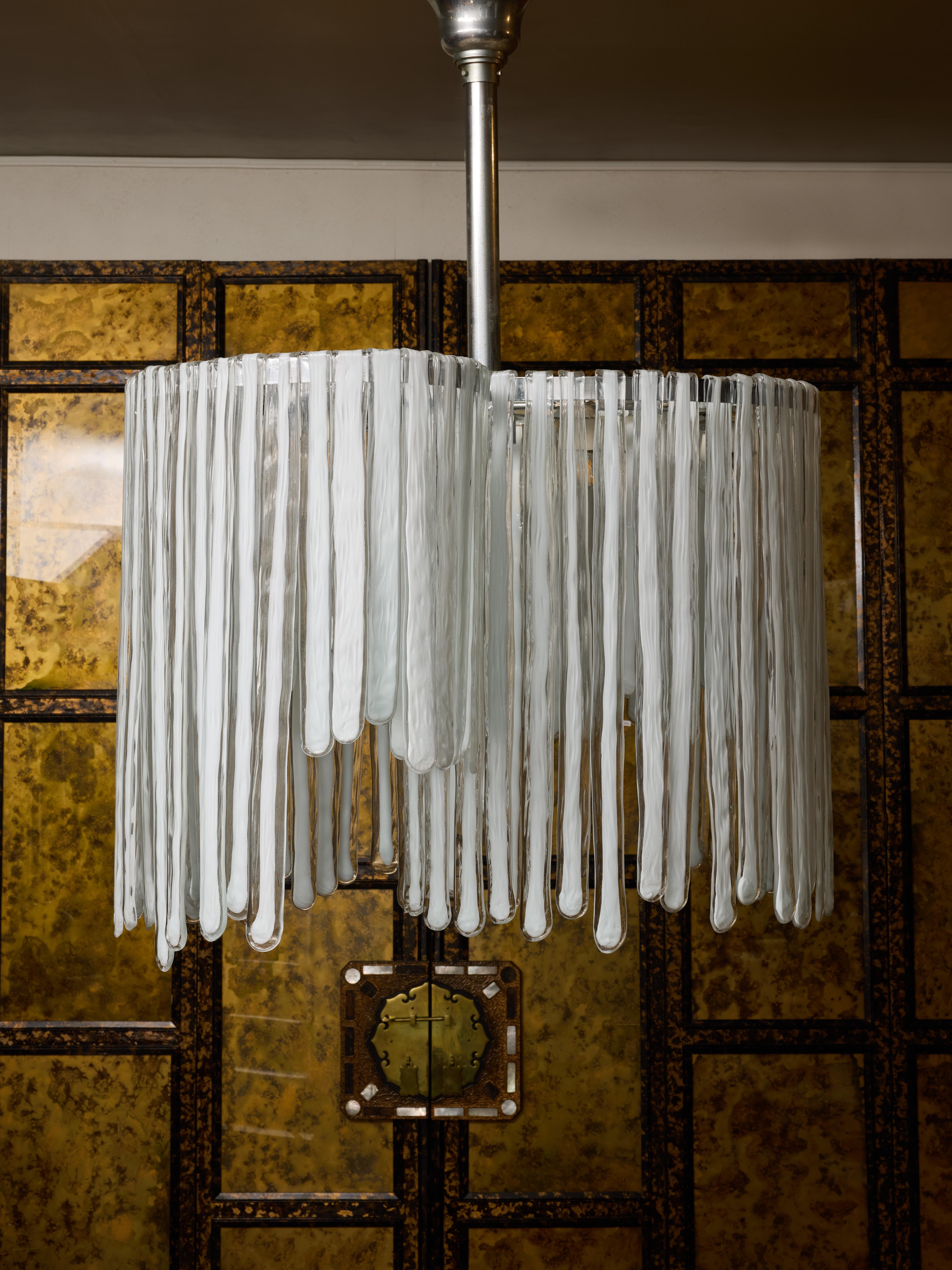 Lampadario vintage composto da una struttura in metallo da cui pendono decine di lastre di vetro di Murano trasparente fatte a mano con il bianco al centro, piegate in alto in modo da agganciarsi direttamente alla struttura.

Questo lampadario è a