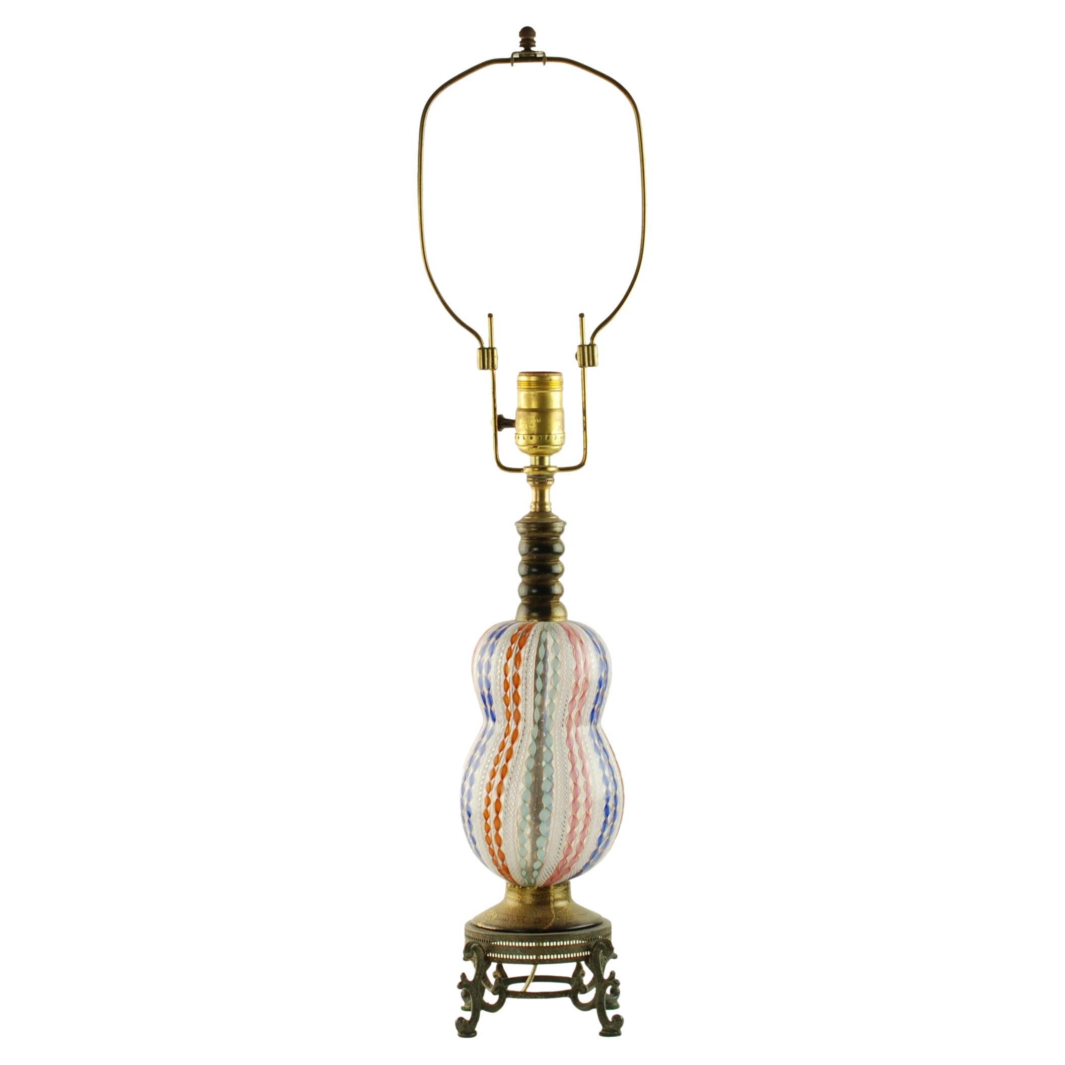 This handblown Italian Murano glass table lamp has an organic double gourd or squash form which rests upon a black glass pedestal base decorated with gold wash. The body of the piece features white zanfirico decoration alternating with multicolored