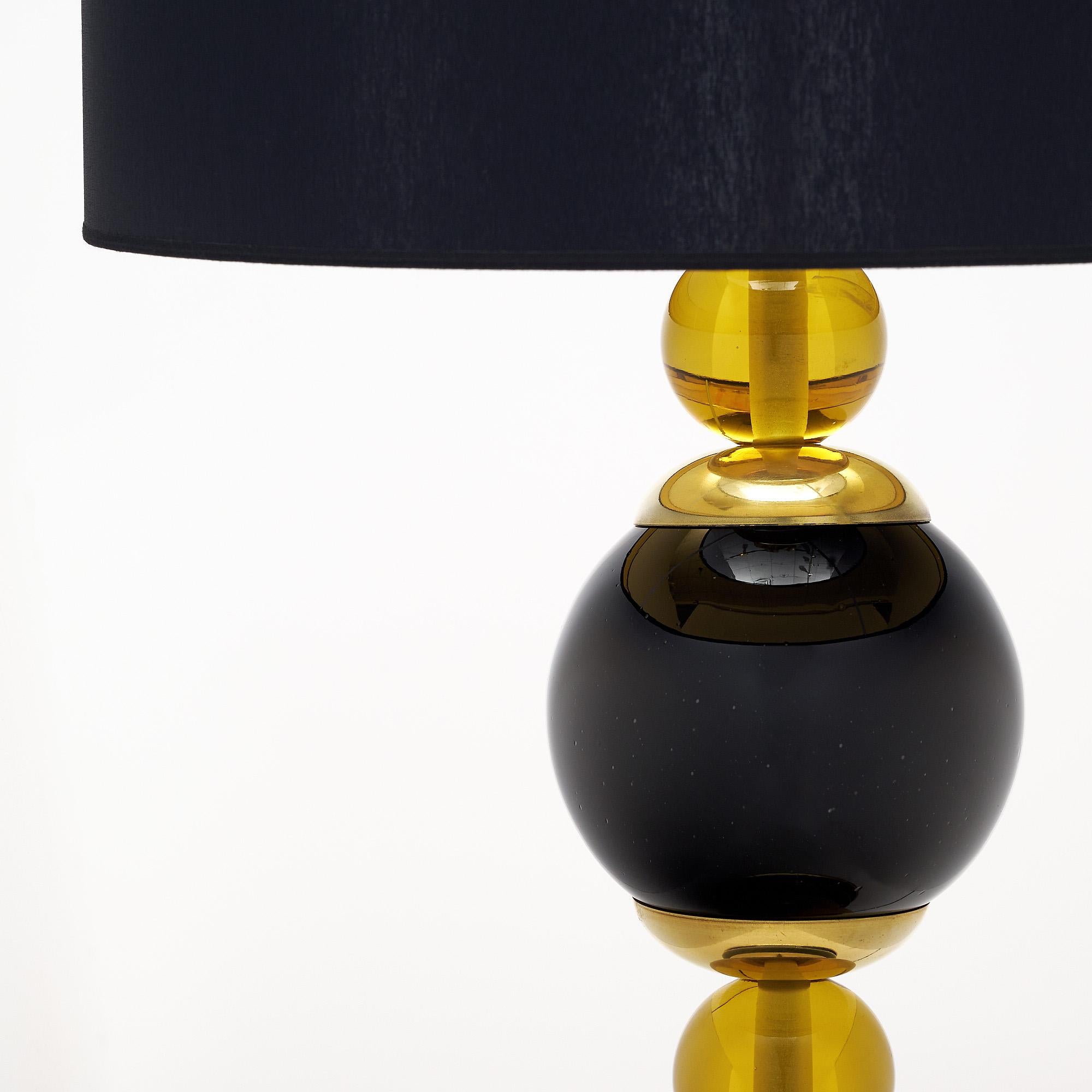 A pair of Murano glass table lamps featuring two black glass spheres and two clear amber smaller spheres combined together to form the stem of each lamp. They are enhanced with gilt brass cups and sit on a strong gilt brass and black glass base.