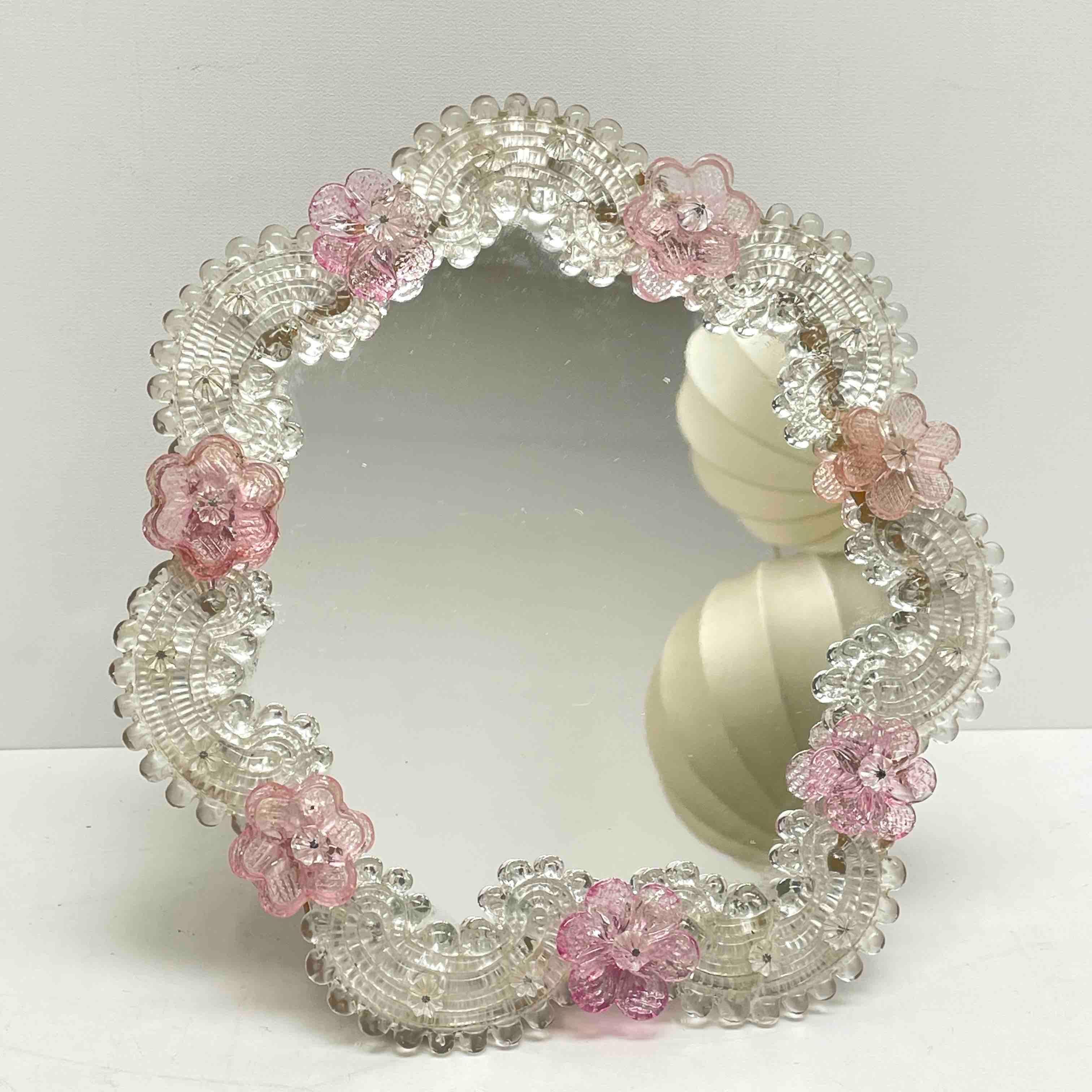 A gorgeous Murano glass vanity mirror surrounded with handmade light pink flowers. Can be used as a wall mirror or standing mirror. With minor signs of wear as expected with age and use. A nice addition to any girls or ladies room. Its stands about