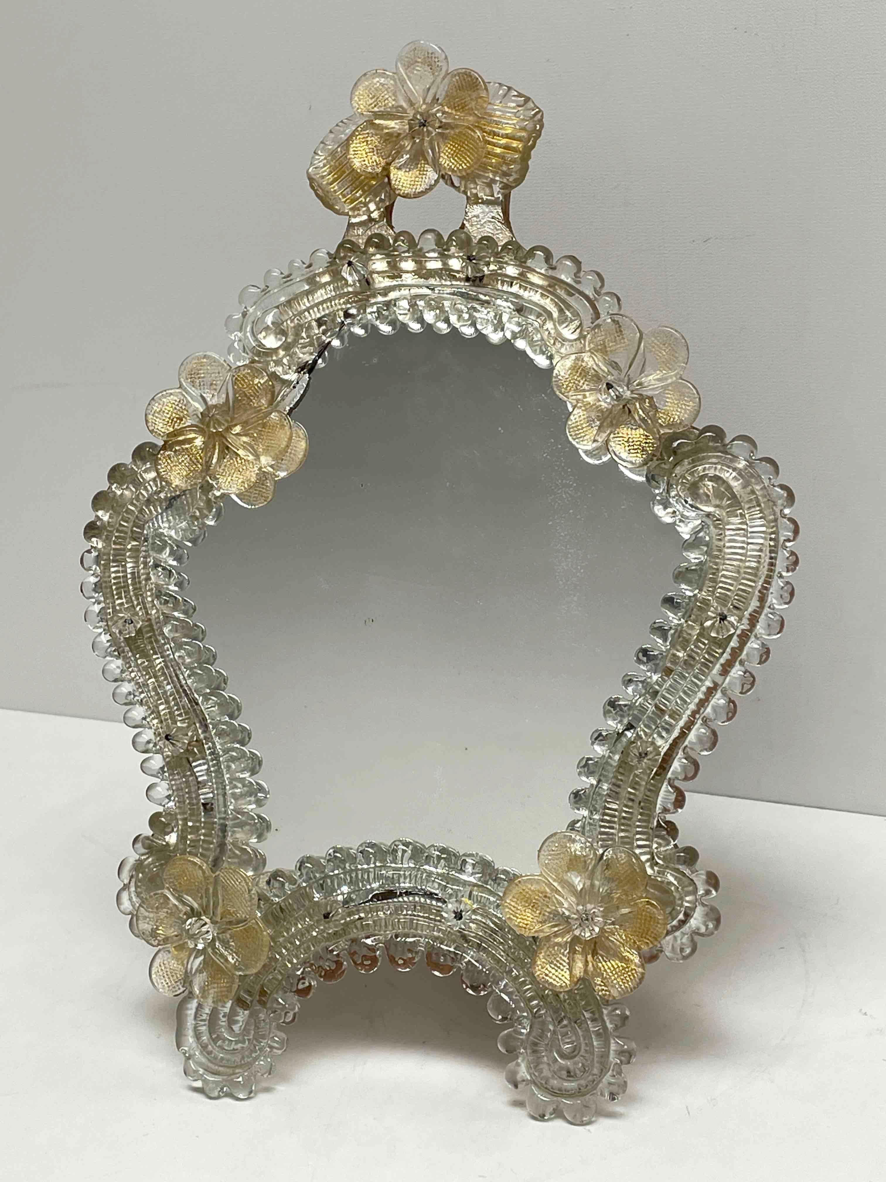 A gorgeous Murano glass vanity mirror surrounded with handmade clear gold flake flowers. Can be used as a wall mirror or standing mirror. With minor signs of wear as expected with age and use. A nice addition to any girls or ladies room. Its stands