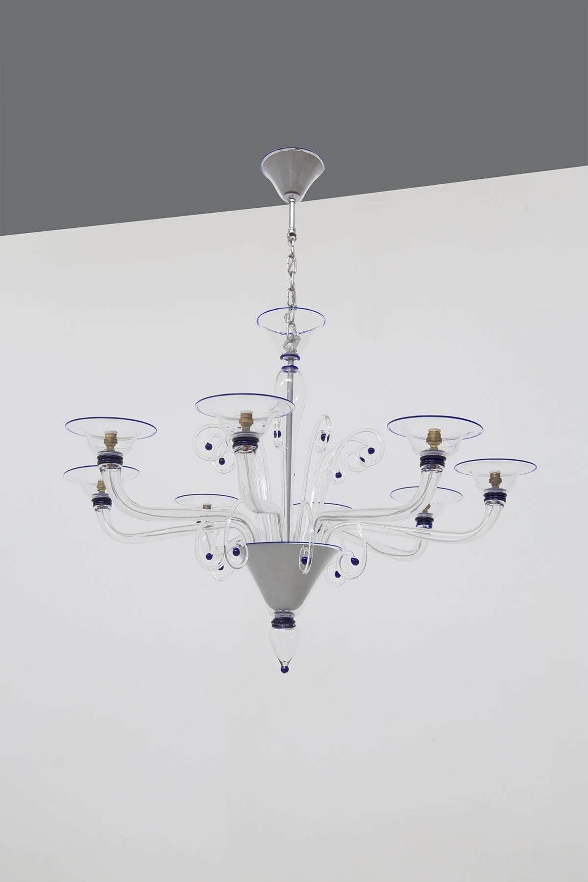 The splendid vintage chandelier is made in the ‘60s with Murano glass. 
The whole aluminum structure is encased in an elegant and sumptuous glass. The lower conic conical shape there are 8 curved arms that each hold a light bulb. The arms widen and