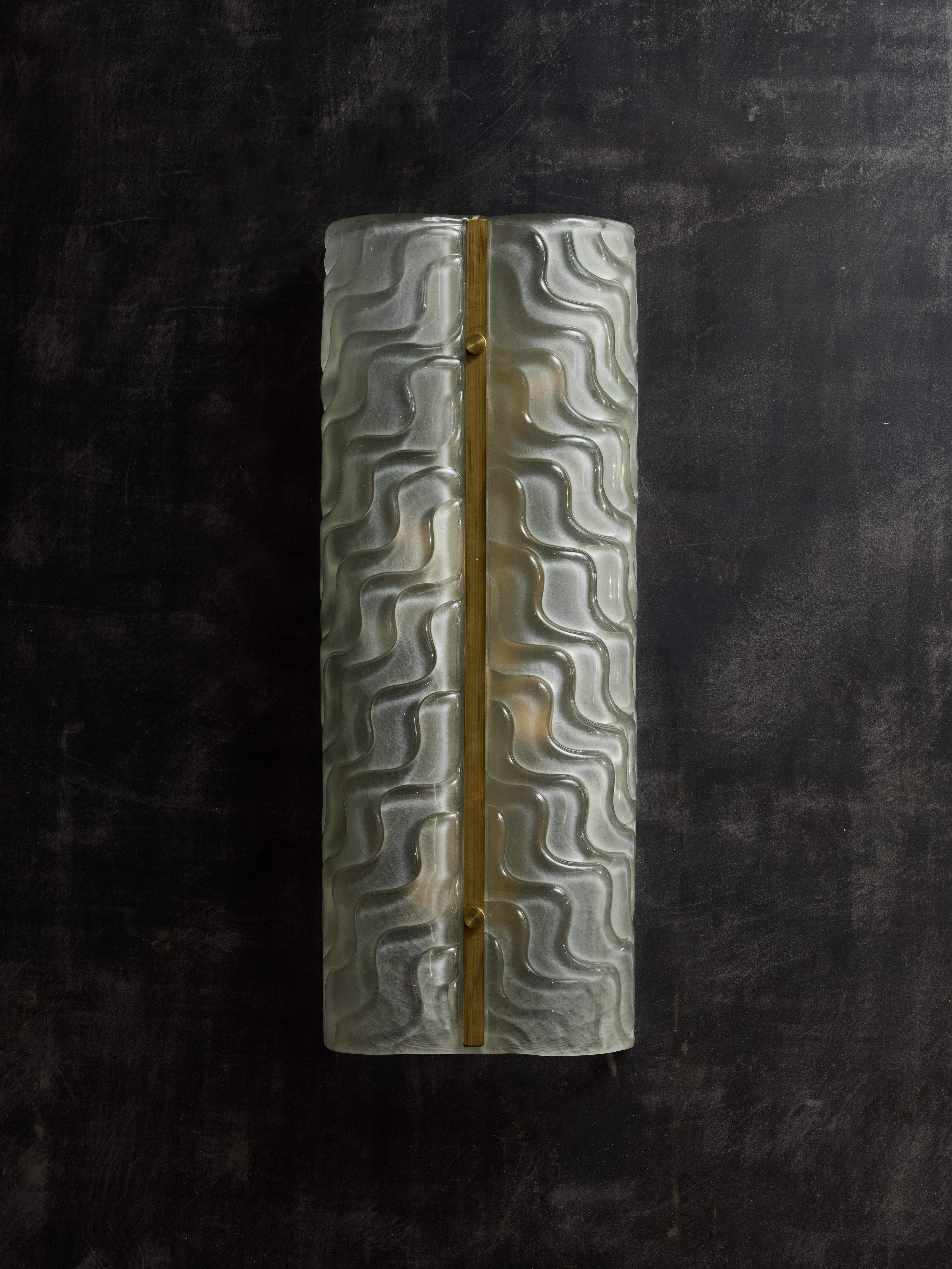 Murano glass wall sconce made of a curved panel, slightly frosted with wavy pattern reflecting on both sides. In the center is a unlacquered brass stem giving the final touch to this decorative piece.
Four sources of light  per sconce