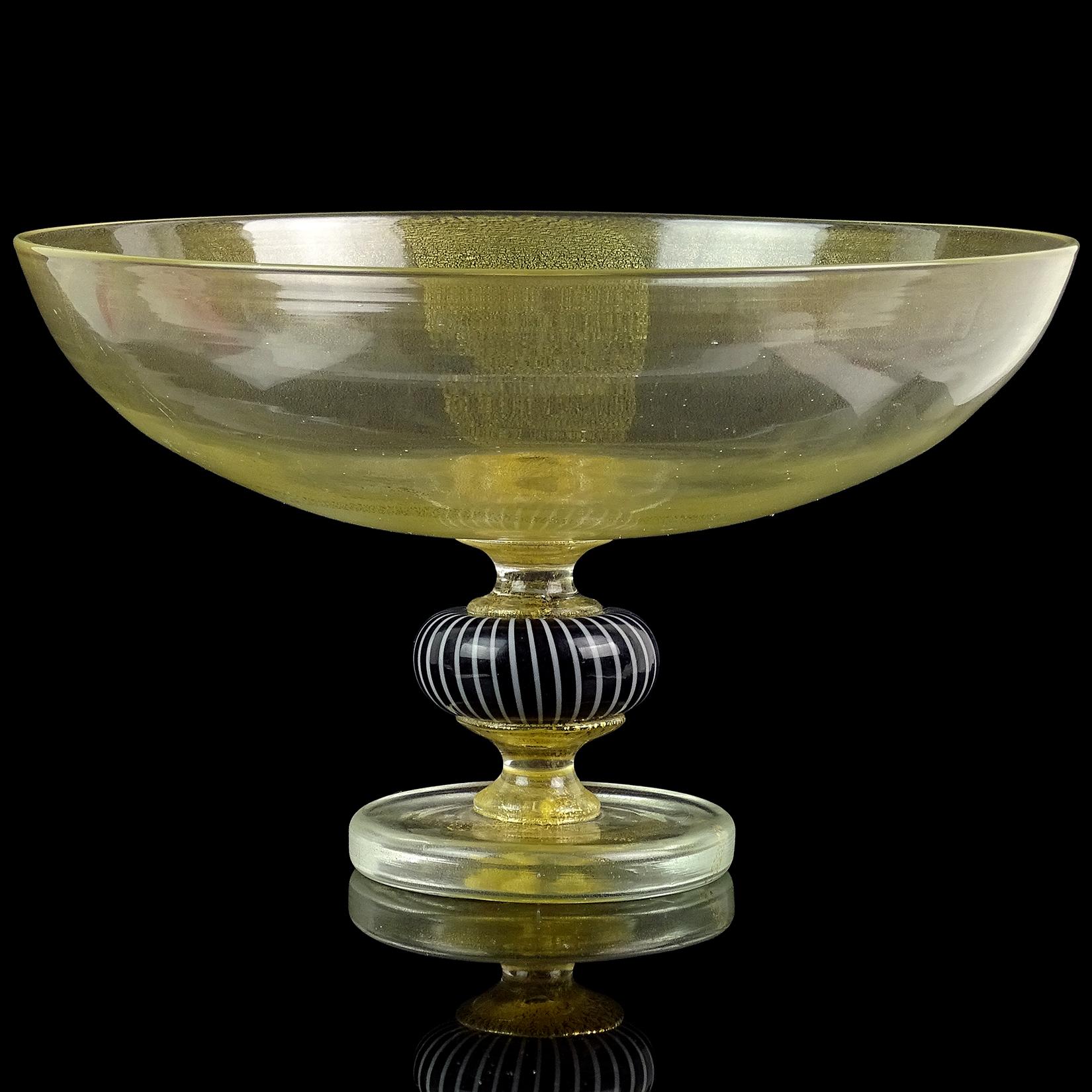 Beautiful vintage Murano hand blown gold flecks Italian art glass footed compote / centerpiece bowl. The bowl has an applied foot, with black and white center decoration that attaches the top and bottom. The bowl is profusely covered in gold leaf.