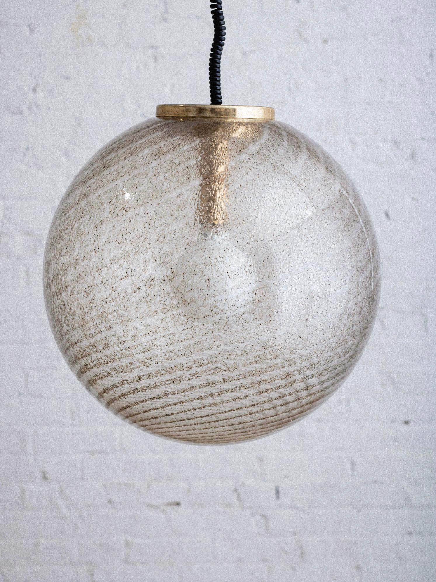 A mid century Murano glass pendant light. Speckled gold swirl shimmers through the clear glass. Brass hardware and black spiral cord. Original ceiling canopy included. Wire adds 26” to height. Sourced in Northern Italy.