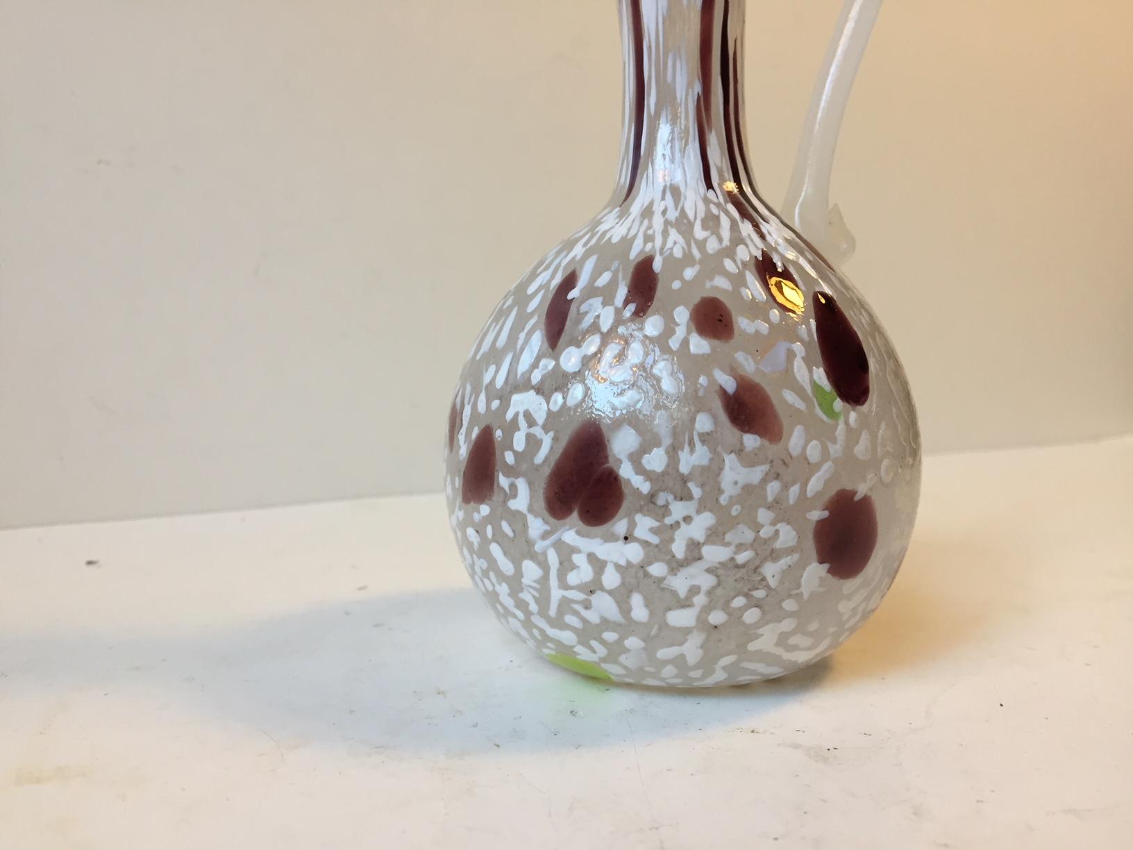 This decorative Murano vase is shaped like a small jug. It displays a 'Fazzoletto' technique where the white background color is made from thousands of air bubbles. Possibly designed by Napoleone Martinuzzi.