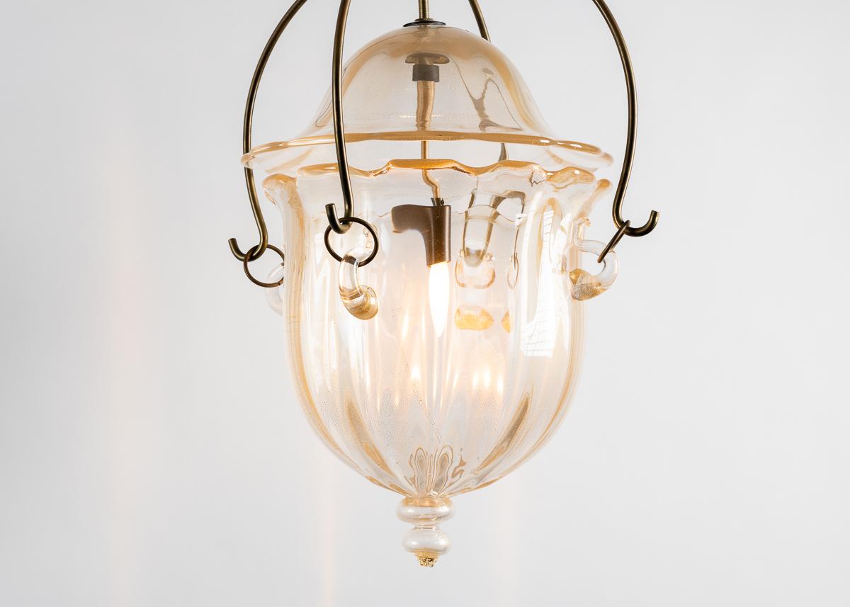 A beautiful Murano lamp with flared details, a brass chain and canopy and a subtly hued glass shade which, with it's lower half, intimates the shape of water condensing into a droplet.