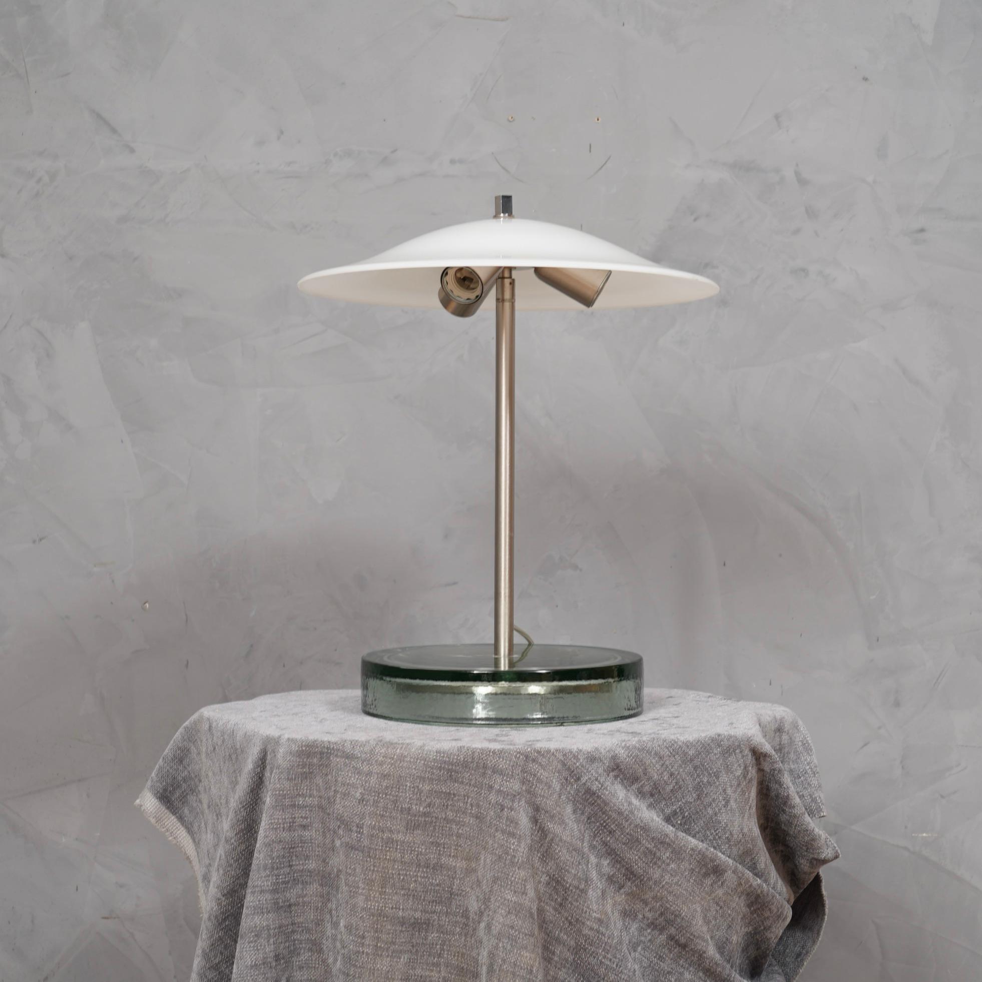 Ein unverwechselbares Design für diese Tischlampen von Vistosi, sicherlich sehr elegant auf einem schönen Schreibtisch.

Die Lampe besteht aus einem großen, transparenten Glassockel, aus dem in der Mitte ein satinierter Stahlstiel herausragt, an dem
