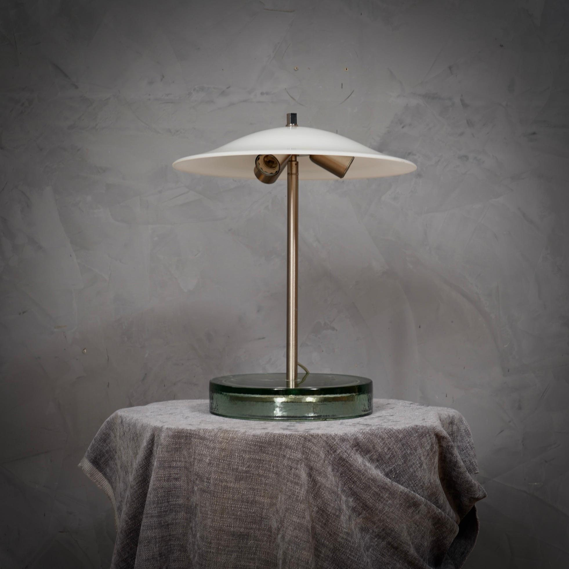 Diseño inconfundible para estas lámparas de mesa de Vistosi, sin duda muy elegantes sobre un hermoso escritorio.

La lámpara está formada por una gran base de cristal transparente de la que sale centralmente un vástago de acero satinado en el que se