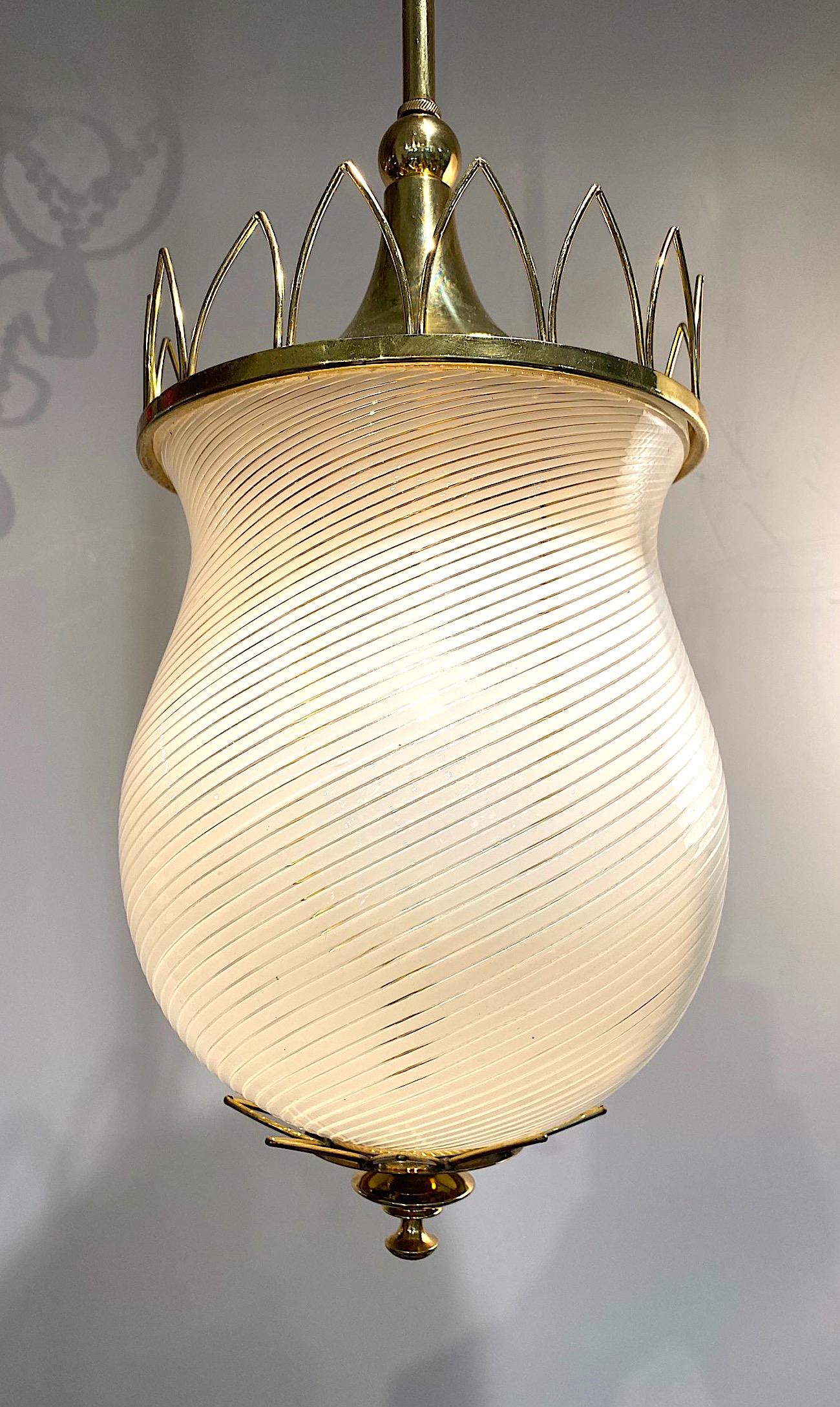 Charming late 1940s to mid 1950s Italian pendant light in brass and glass. The vase shape shade is hand blown Murano glass in clear and white stripe. The lantern is brass that is newly polished and lacquered. The top brass crown design is nicely