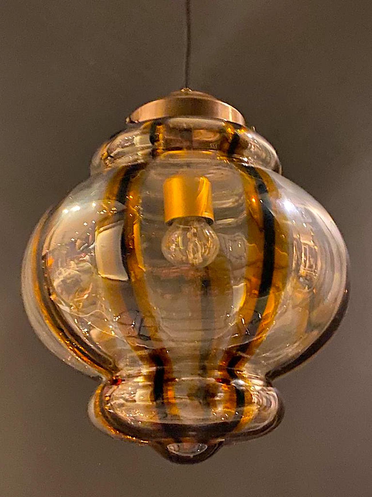 A beautiful hand blow glass pendant light from Murano Italy circa 1970. The shade is blown in clear glass with eight vertical stripes of dark green / black sandwiched between stripes of honey color gold. The shade cap and ceiling canopy are antique