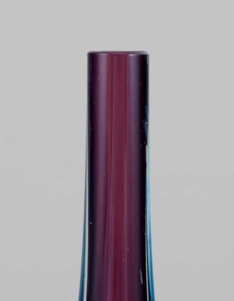 Murano, Italien. Vase aus Kunstglas mit schlankem Hals. 
Blaues und violettes Glas.
Ungefähr 1970.
Label.
Perfekter Zustand.
Abmessungen: H 27,0 cm x B 9,0 cm x T 5,0 cm.