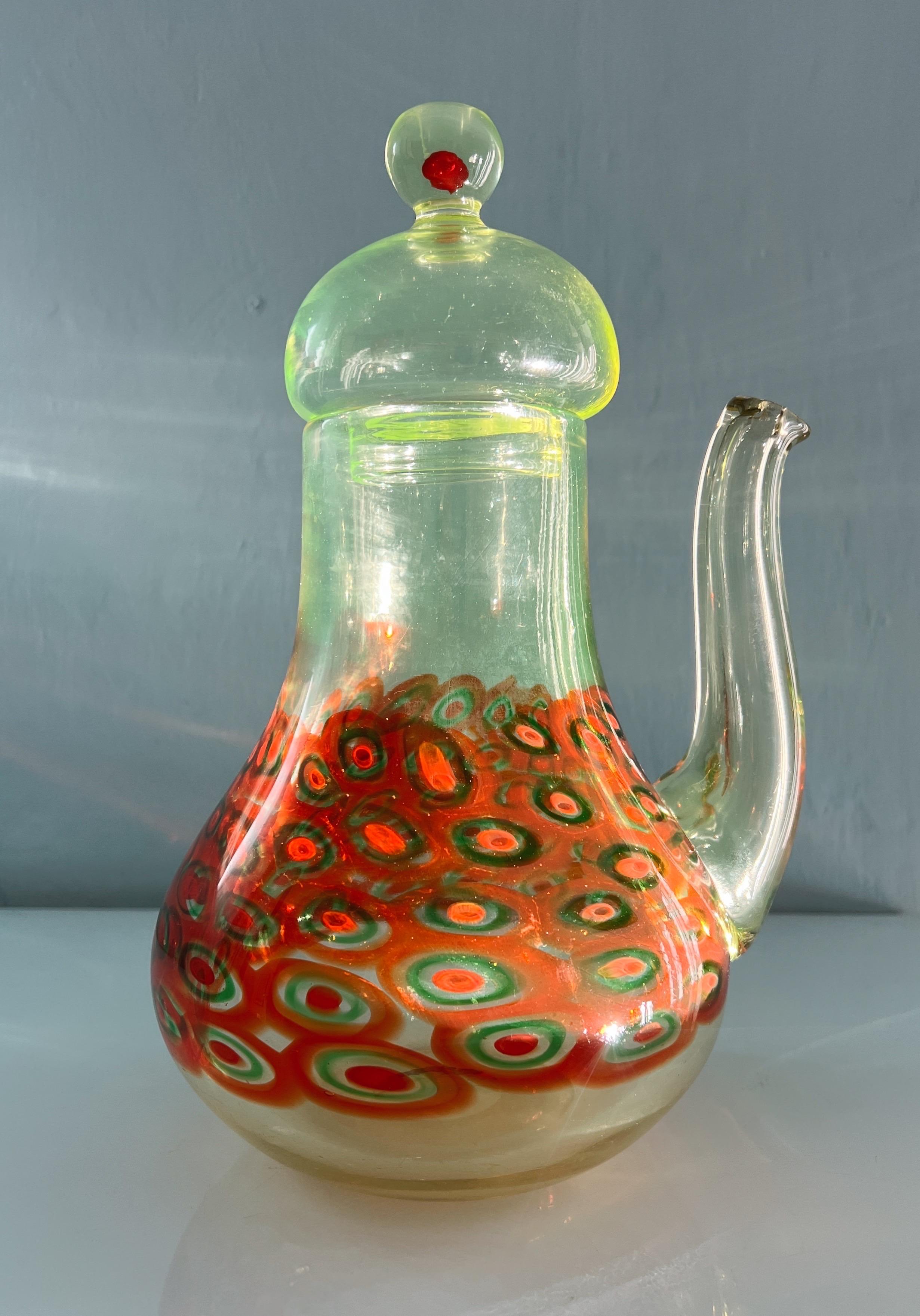 Diese Karaffe aus Murano-Glas ist ein eindrucksvolles Beispiel für italienische Handwerkskunst. Das Design erinnert stark an das klassische Muster von La murrina mit seinen lebhaften Kreisen in Rot, Grün und Weiß, die im unteren Teil des Glases