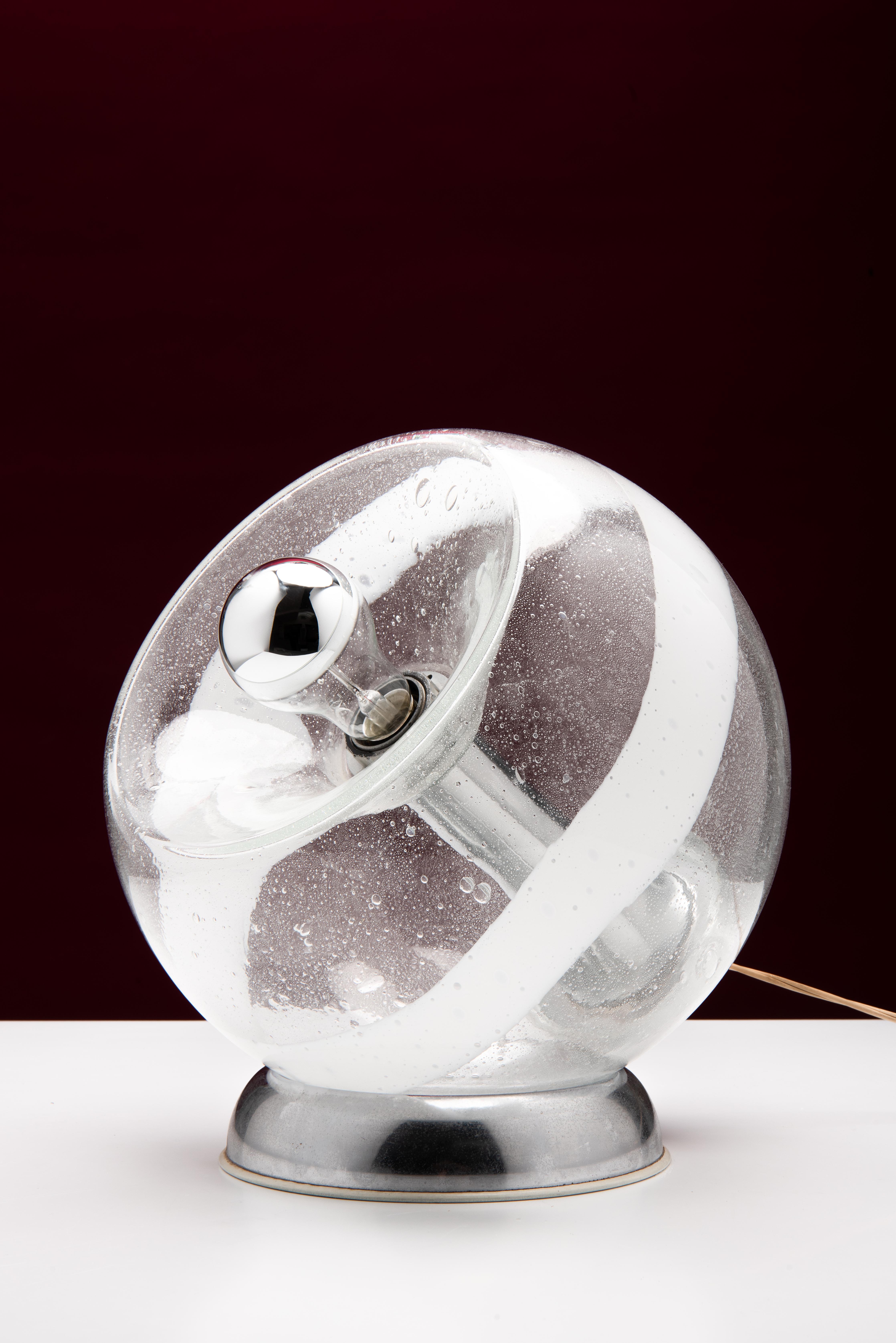 Esta hermosa lámpara de mesa de la Era Espacial, diseñada en los años 60 en Italia, consta de un globo de cristal de Murano transparente con burbujas de aire y un 