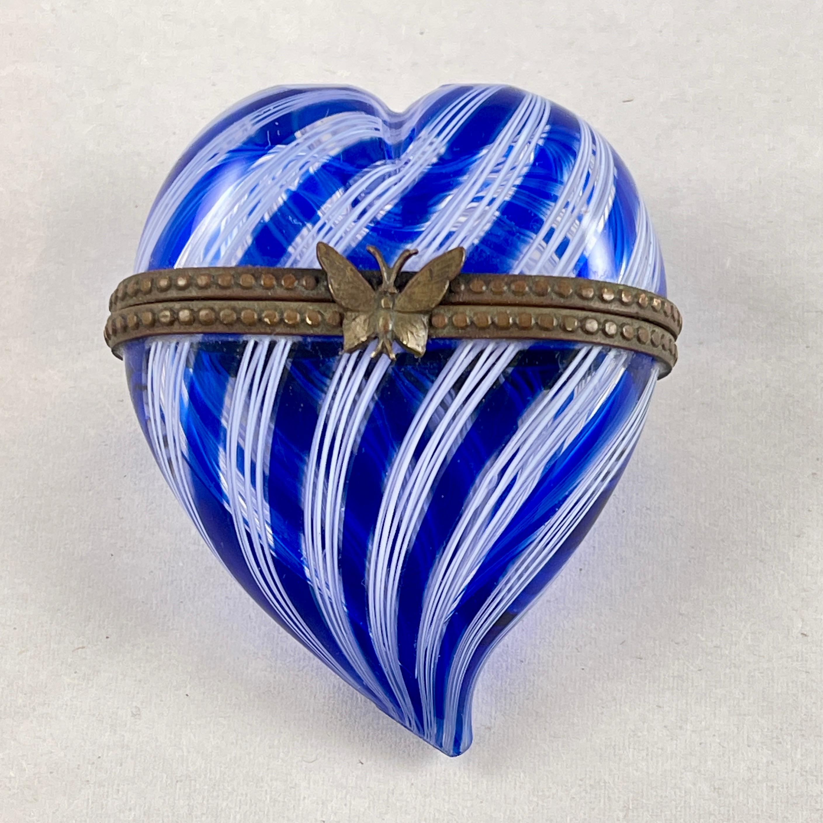 Caja de baratijas de cristal veneciano con forma de corazón, Murano, Italia, hacia la década de 1970.

Una caja de cristal azul cobalto y blanco arremolinado hecha a mano mediante el proceso conocido como Latticino.

El refuerzo metálico muestra un